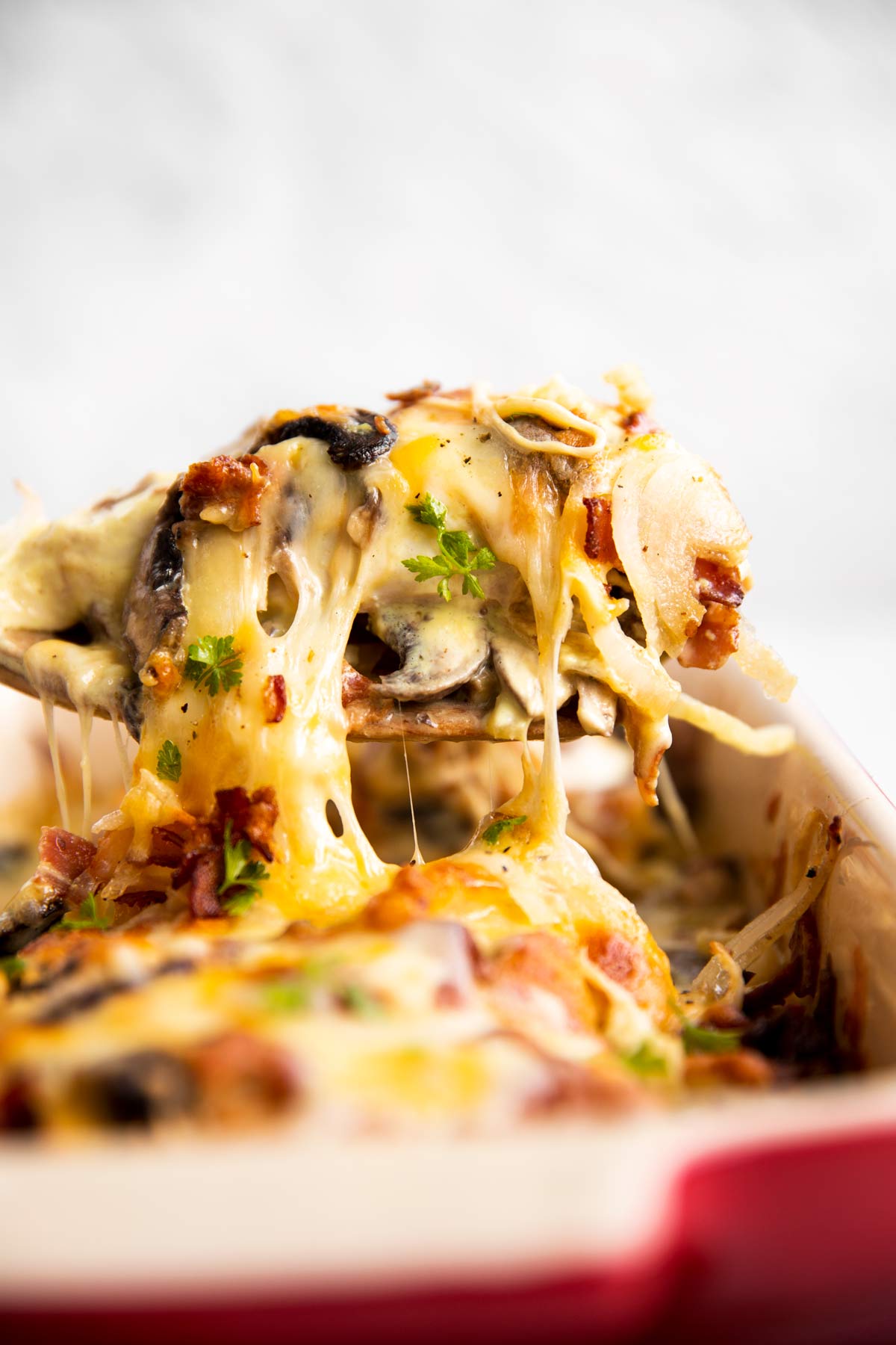 lifting a chicken breast covered with mushrooms and cheese out of a baking dish