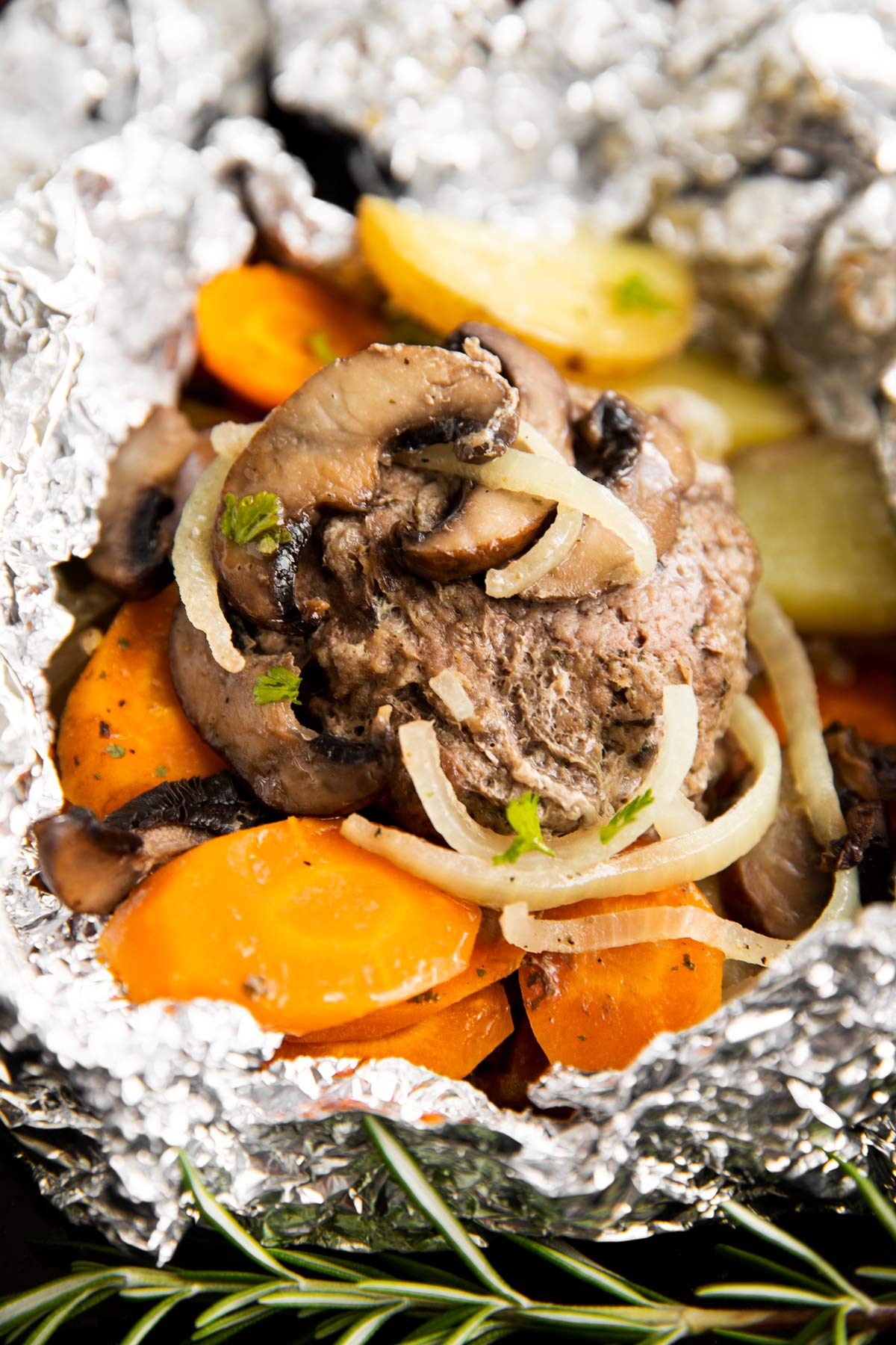 frontal close up of hamburger patty with carrots and potatoes in foil