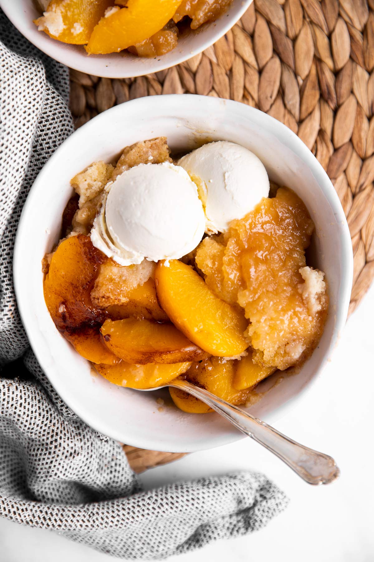 overhead view of white bowl with peach cobbler and ice cream