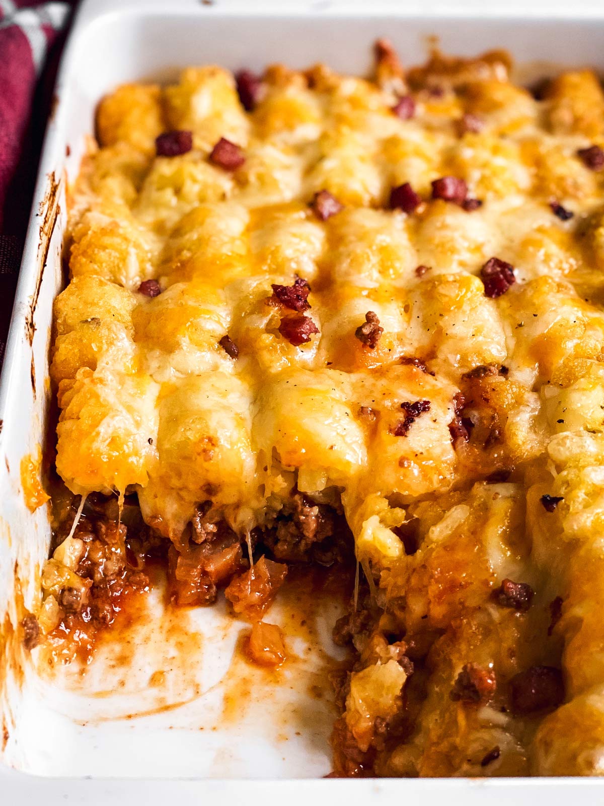 close up photo of bacon cheeseburger tater tot casserole in white baking dish