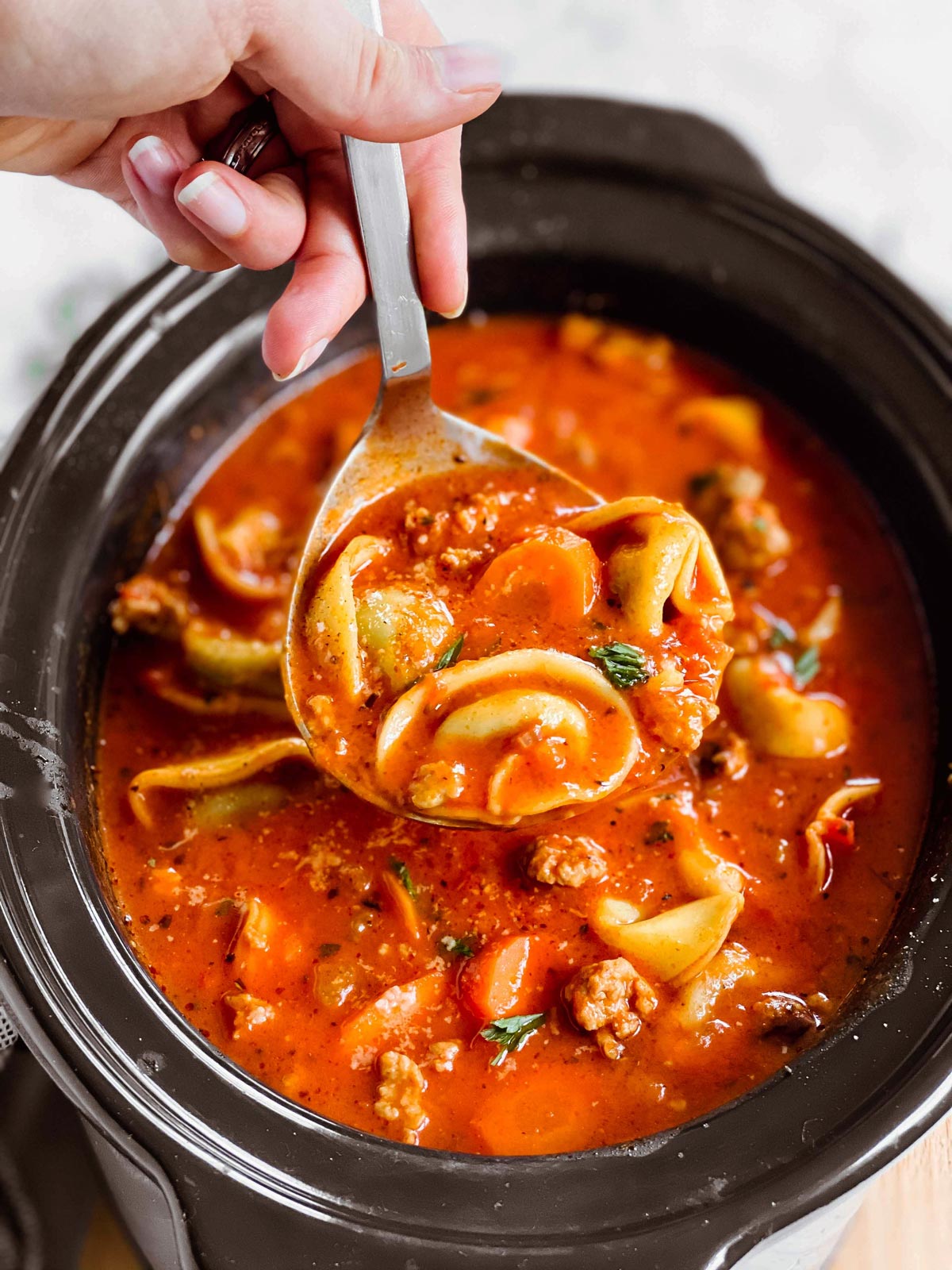 female hand holding ladle filled with tortellini soup