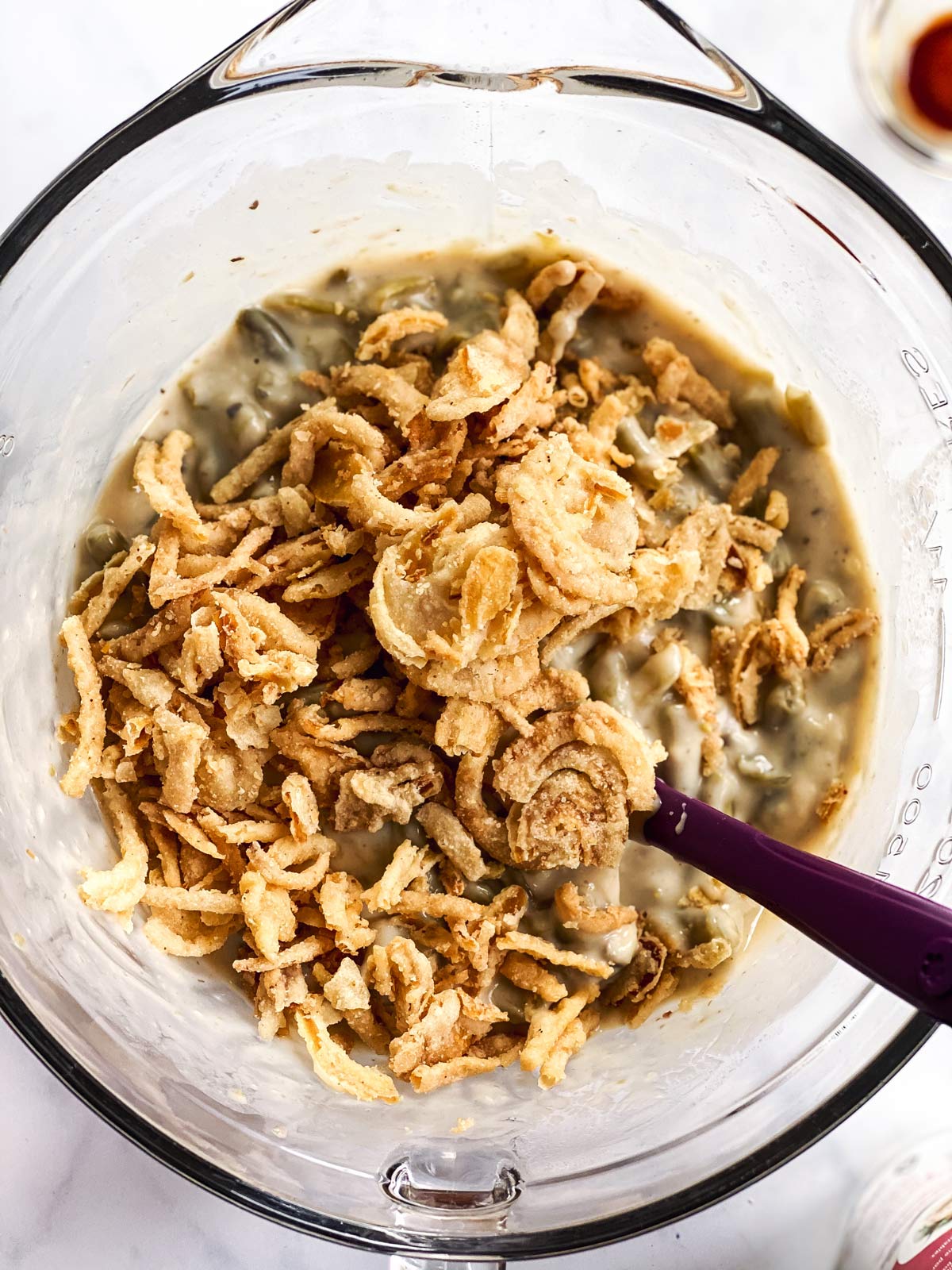 fried onions on top of green bean casserole mixture in glass bowl