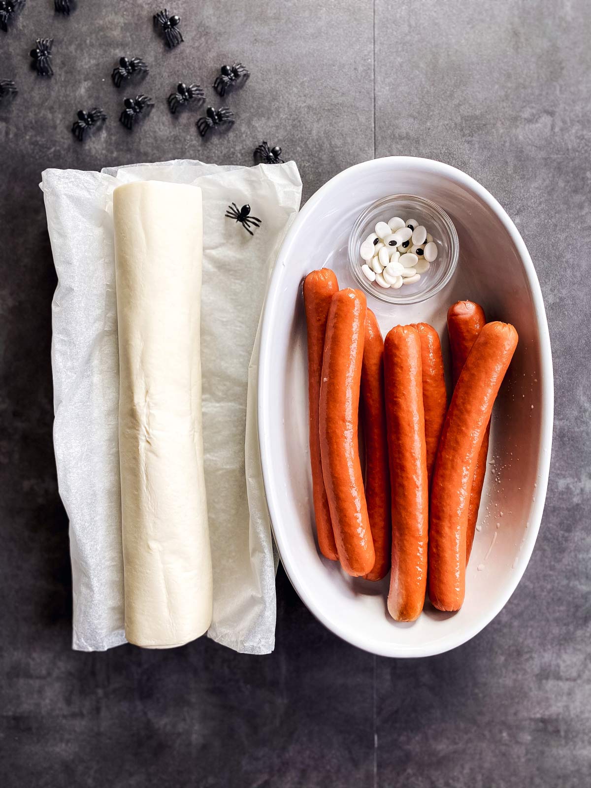 ingredients for mummy decorated hot dogs on a dark background