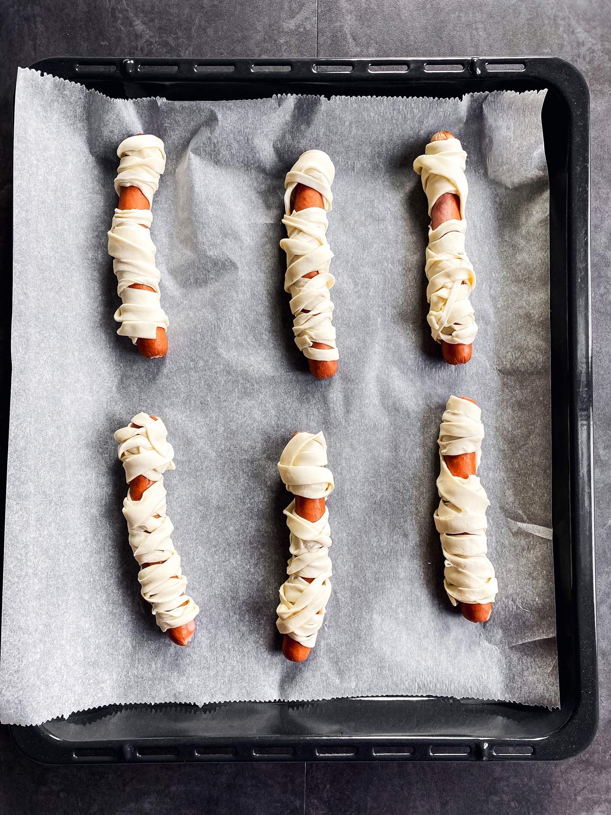 hot dog sausages in puff pastry on lined baking sheet