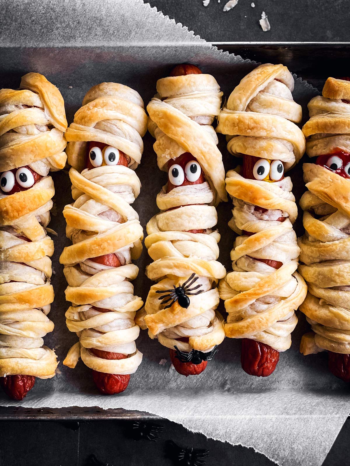 close up of mummy decorated hot dogs on lined baking sheet