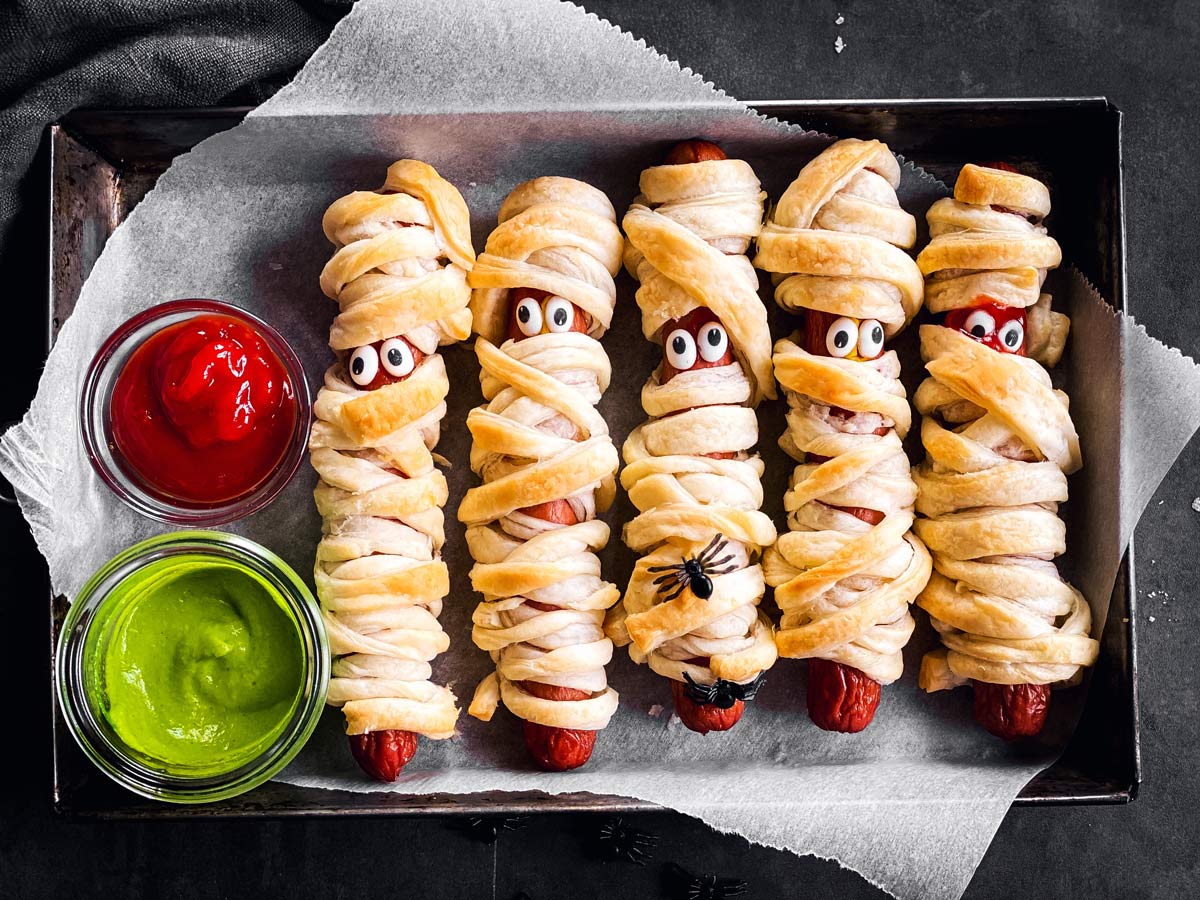 overhead view of small metal pan with mummy hot dogs on dark background