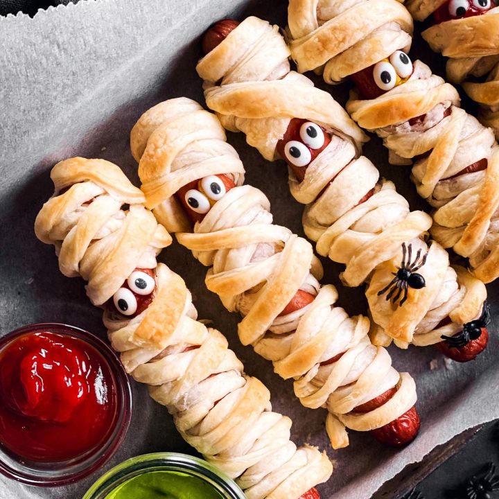 close up overhead view of small metal pan with mummy hot dogs on dark background