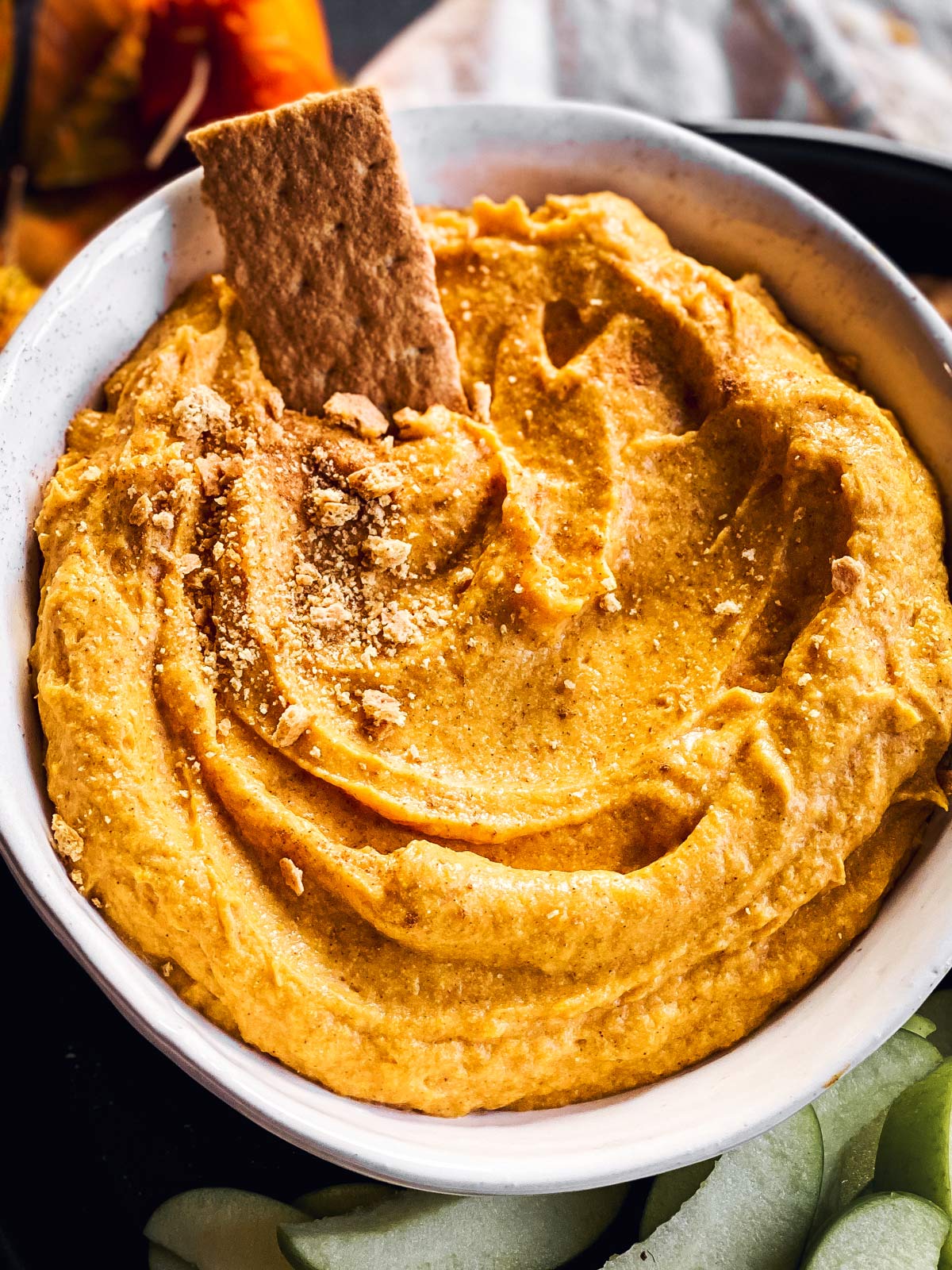 close up of bowl with pumpkin dip and graham cracker stuck in dip