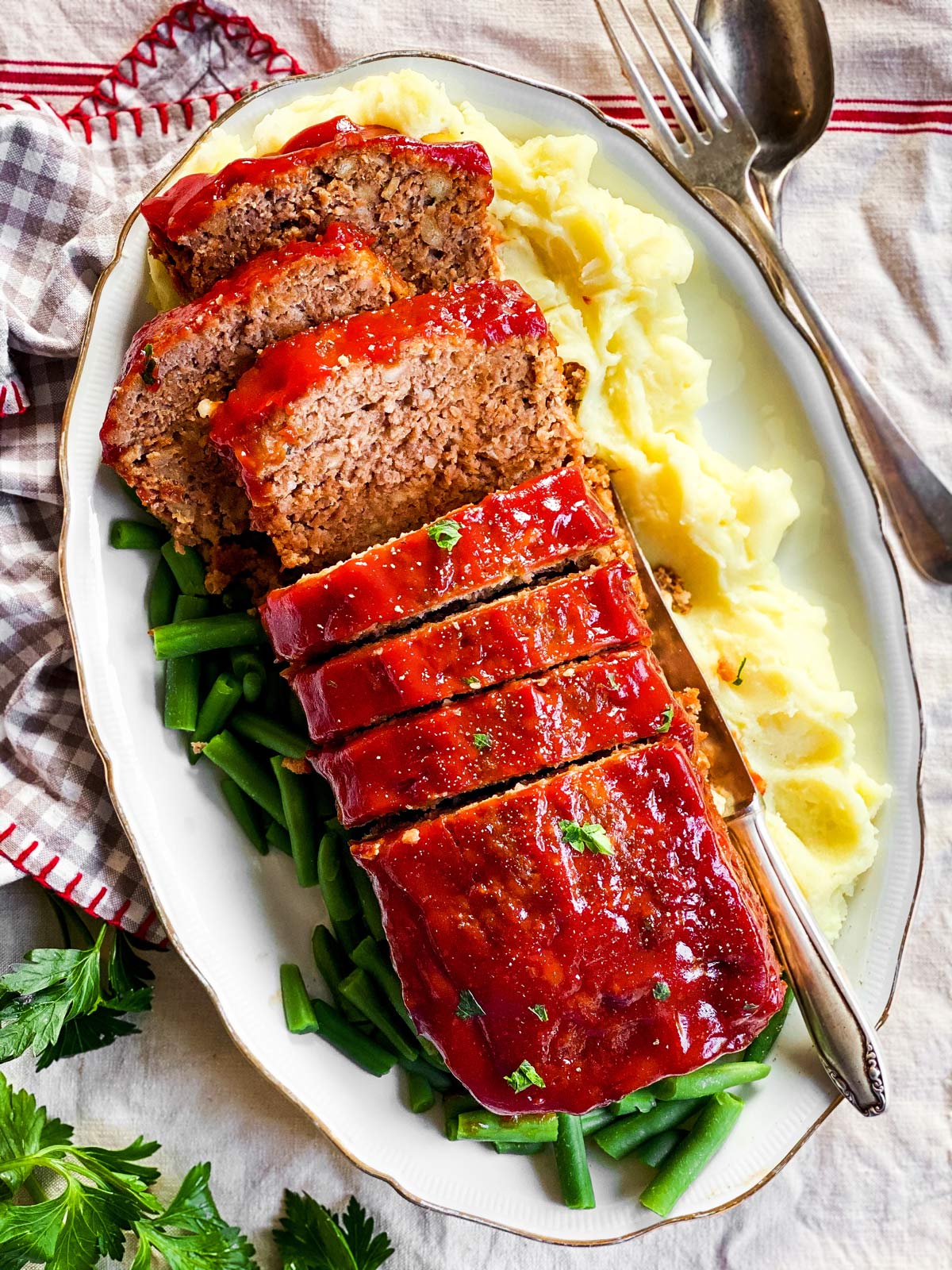 sliced meatloaf on a platter with mashed potatoes and green beans