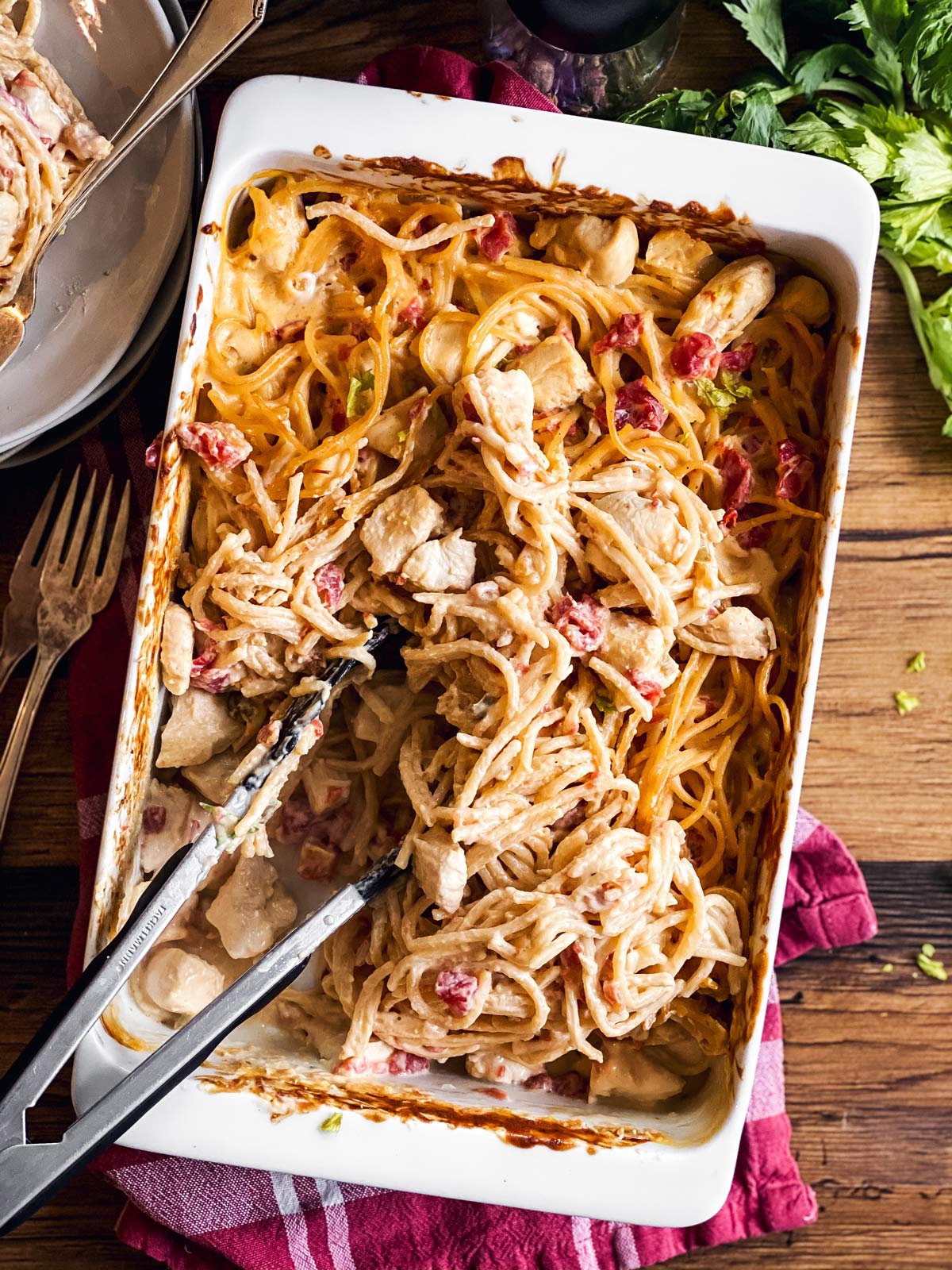 white casserole dish with chicken spaghetti and kitchen tongs on wooden background