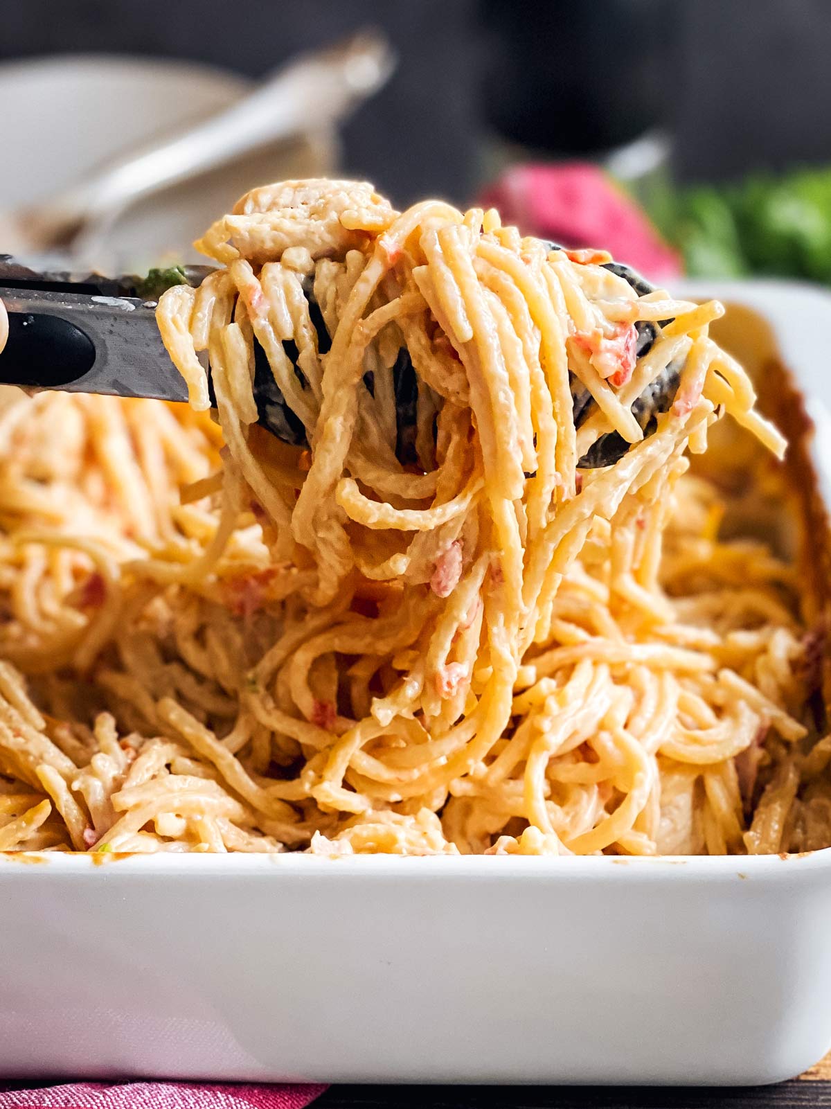 kitchen tongs scooping up chicken spaghetti from dish