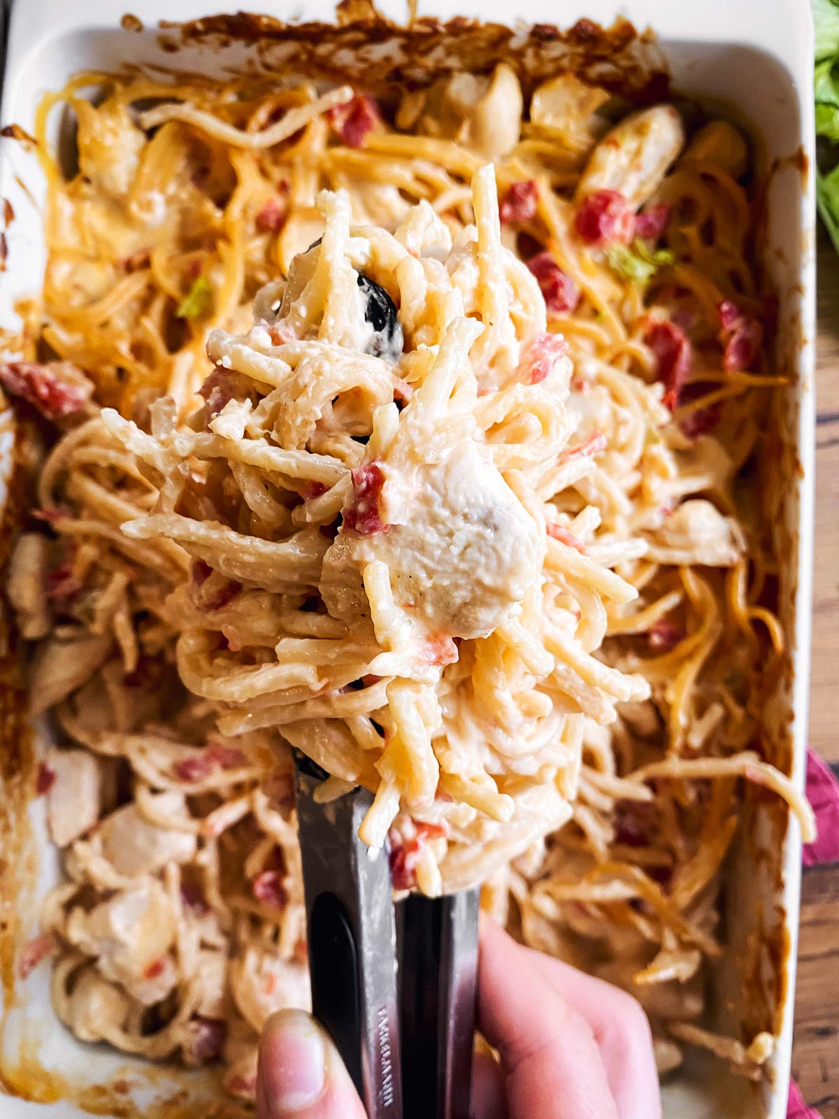 close up of kitchen tongs scooping up chicken spaghetti from dish