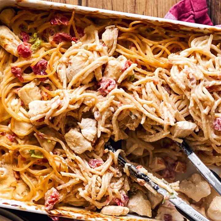 white casserole dish with chicken spaghetti and kitchen tongs on wooden background