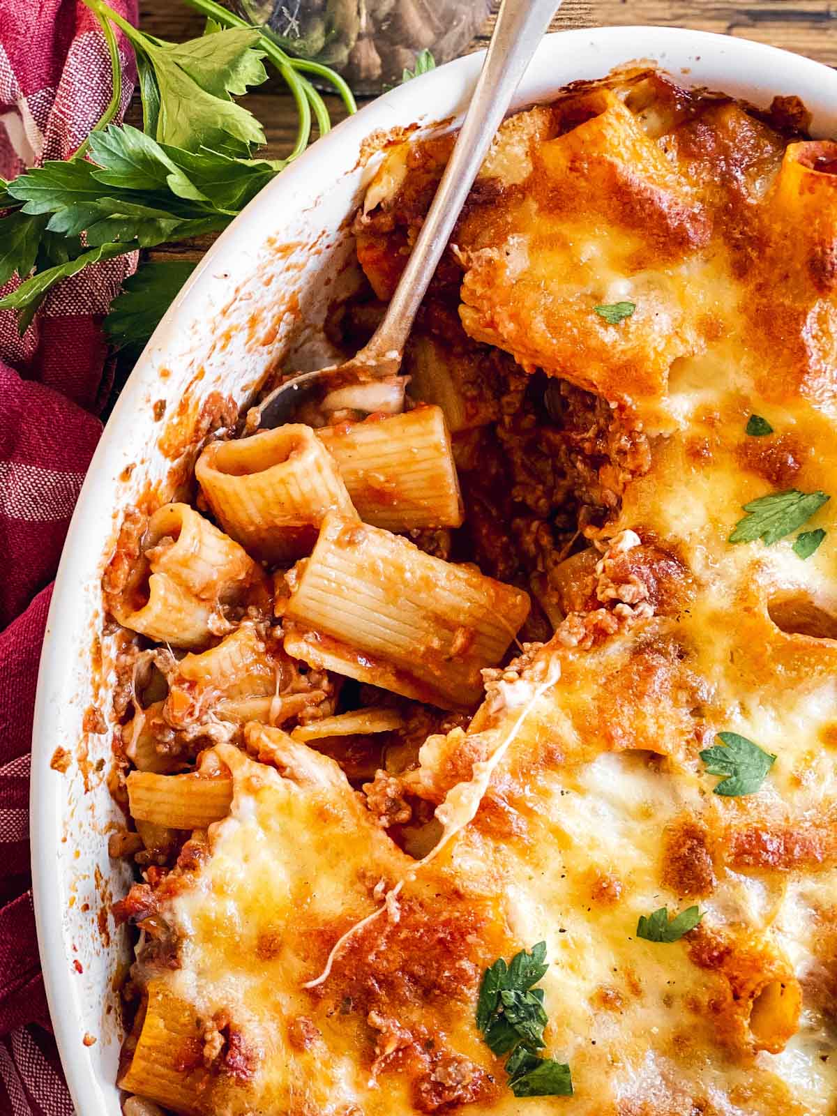 close up photo of spoon scooping out a portion of Rigatoni Bolognese from white casserole dish