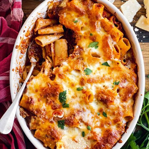 overhead view of baked rigatoni bolognese in white oval casserole dish