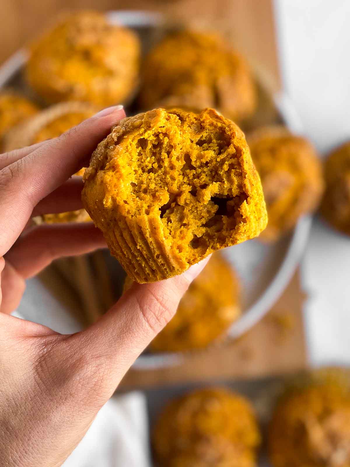 female hand holding half-eaten pumpkin muffin