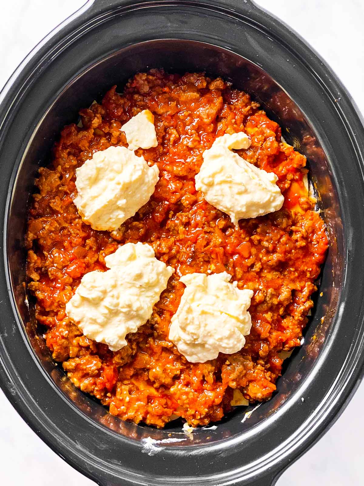 balls of ricotta sauce on top of meat sauce in black crock