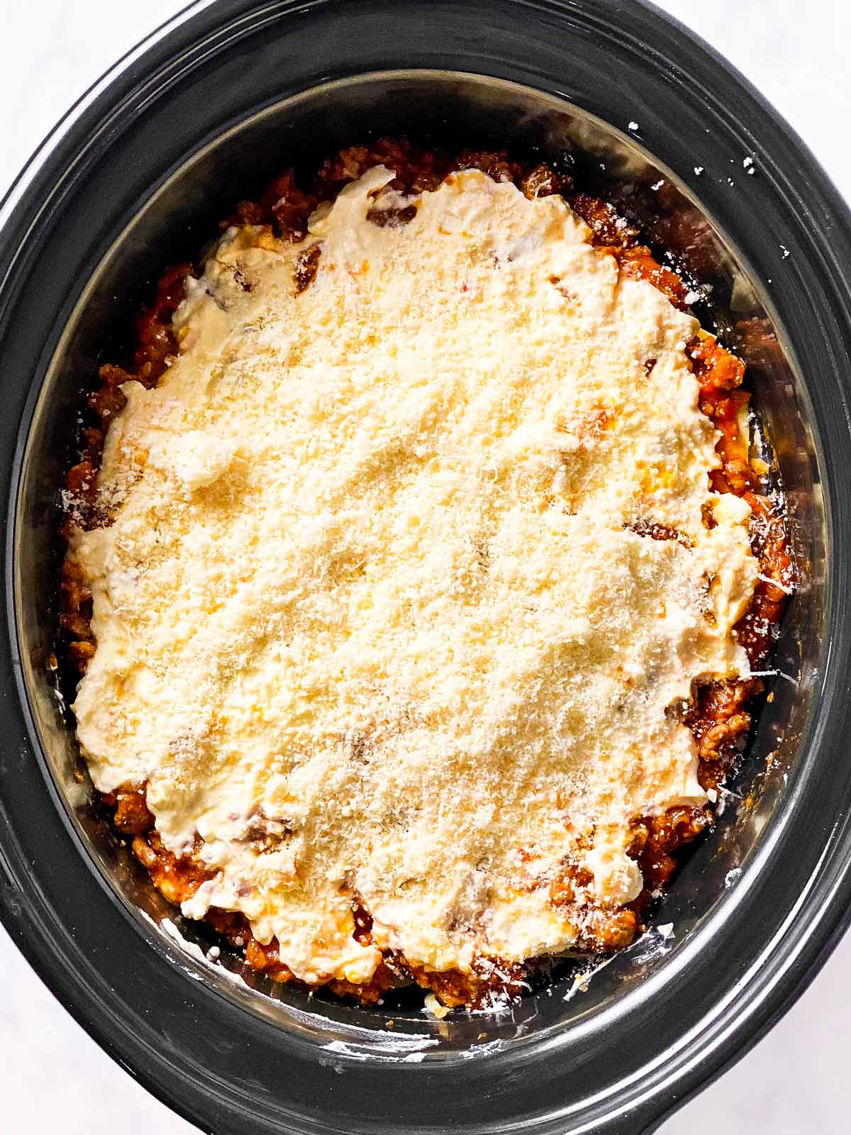 grated parmesan cheese on top of ricotta sauce in black crock