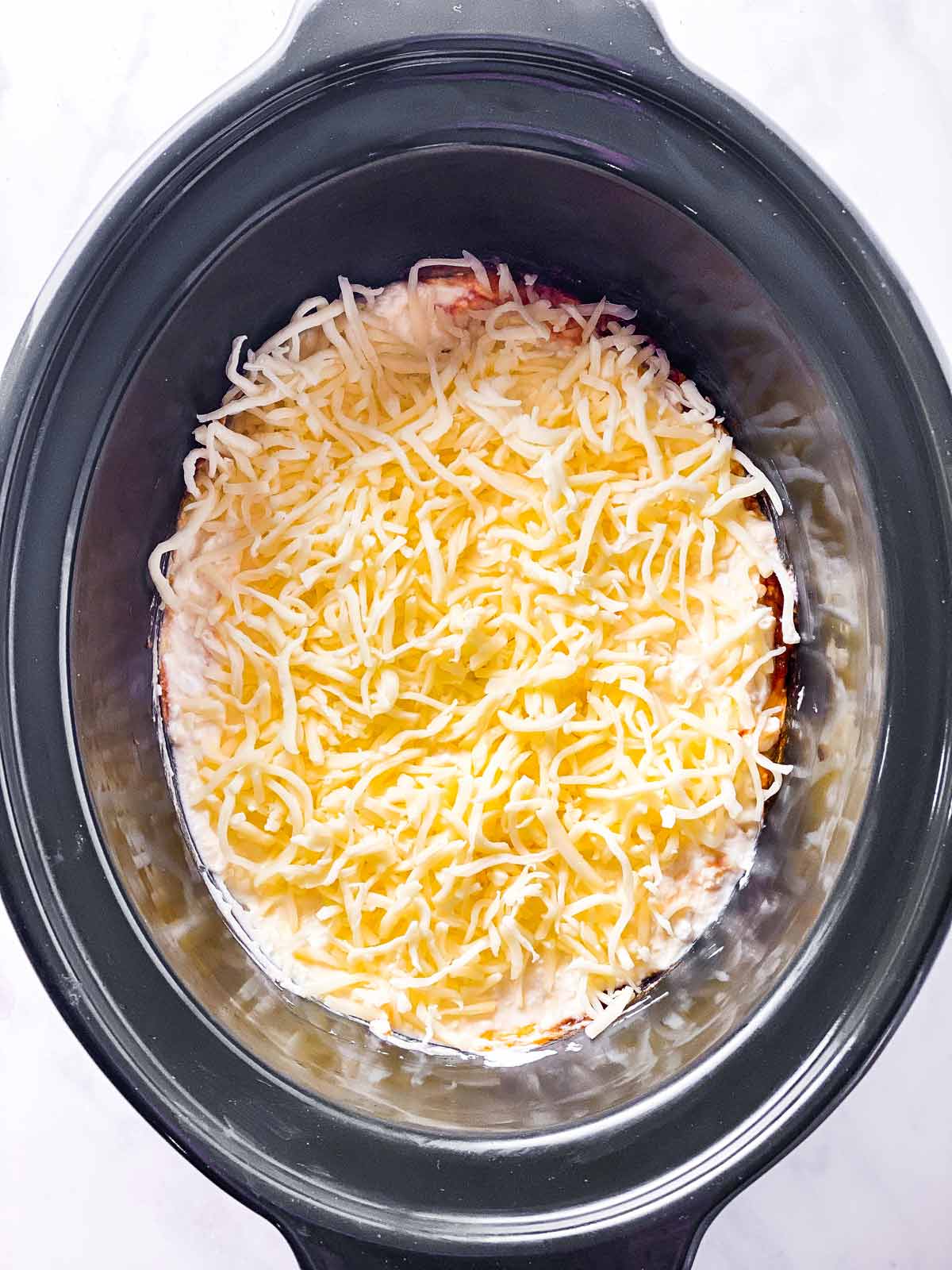shredded mozzarella on top of ricotta sauce in black crock