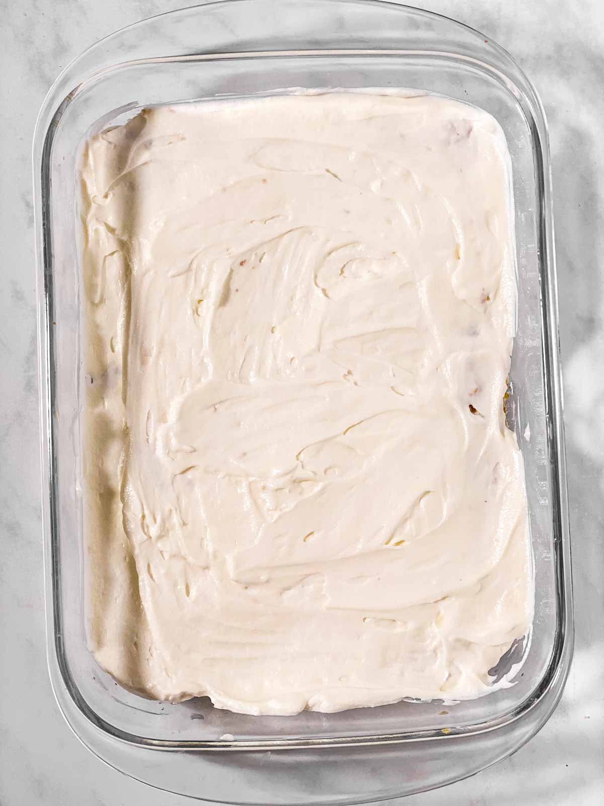 cream spread over cake in glass pan