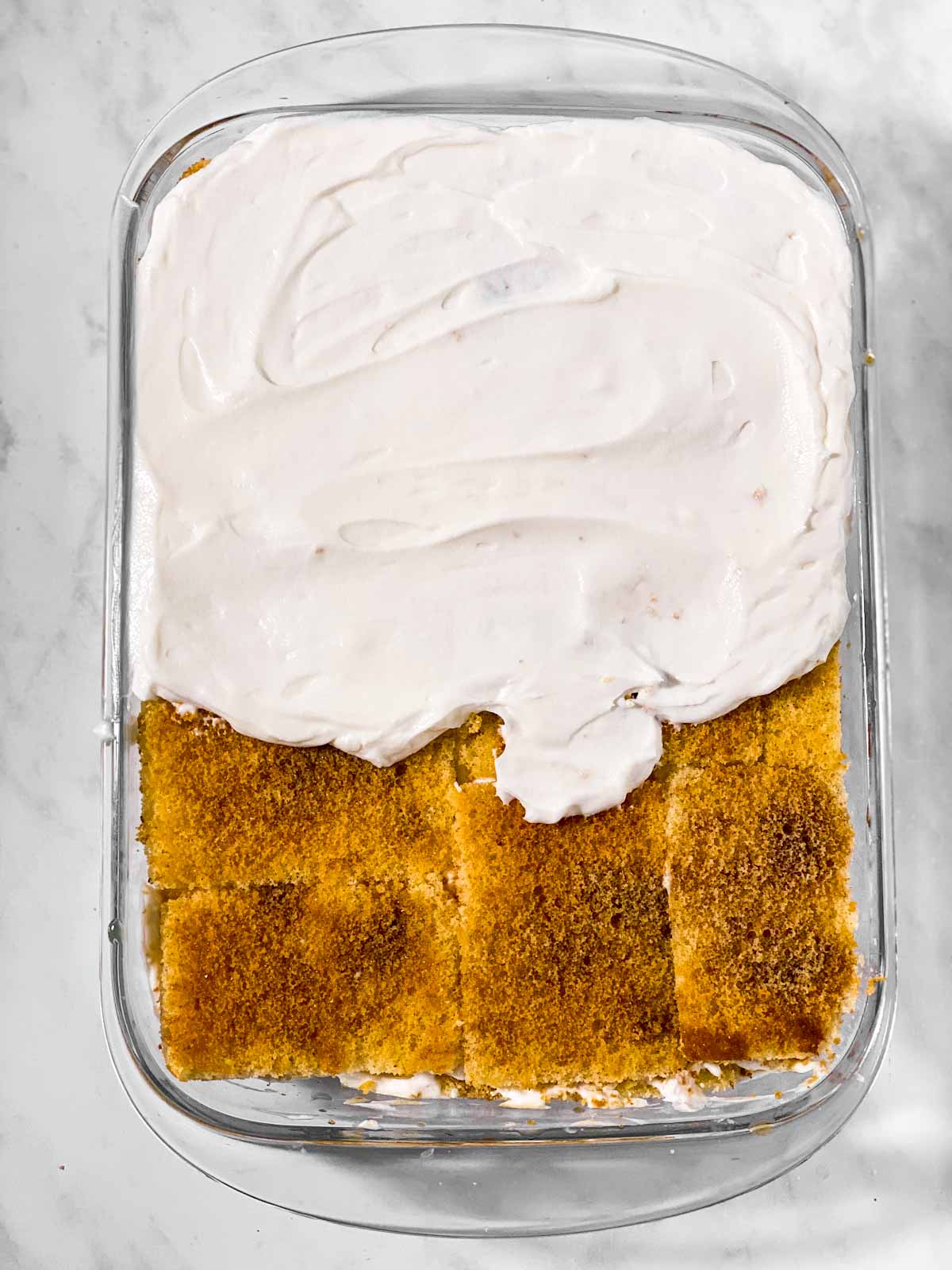 cream mixture half spread over cake layer in glass pan