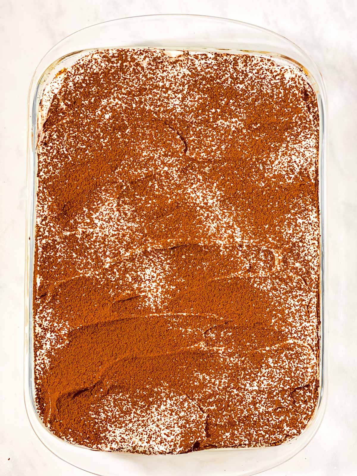 tiramisu dusted with cocoa powder in glass pan