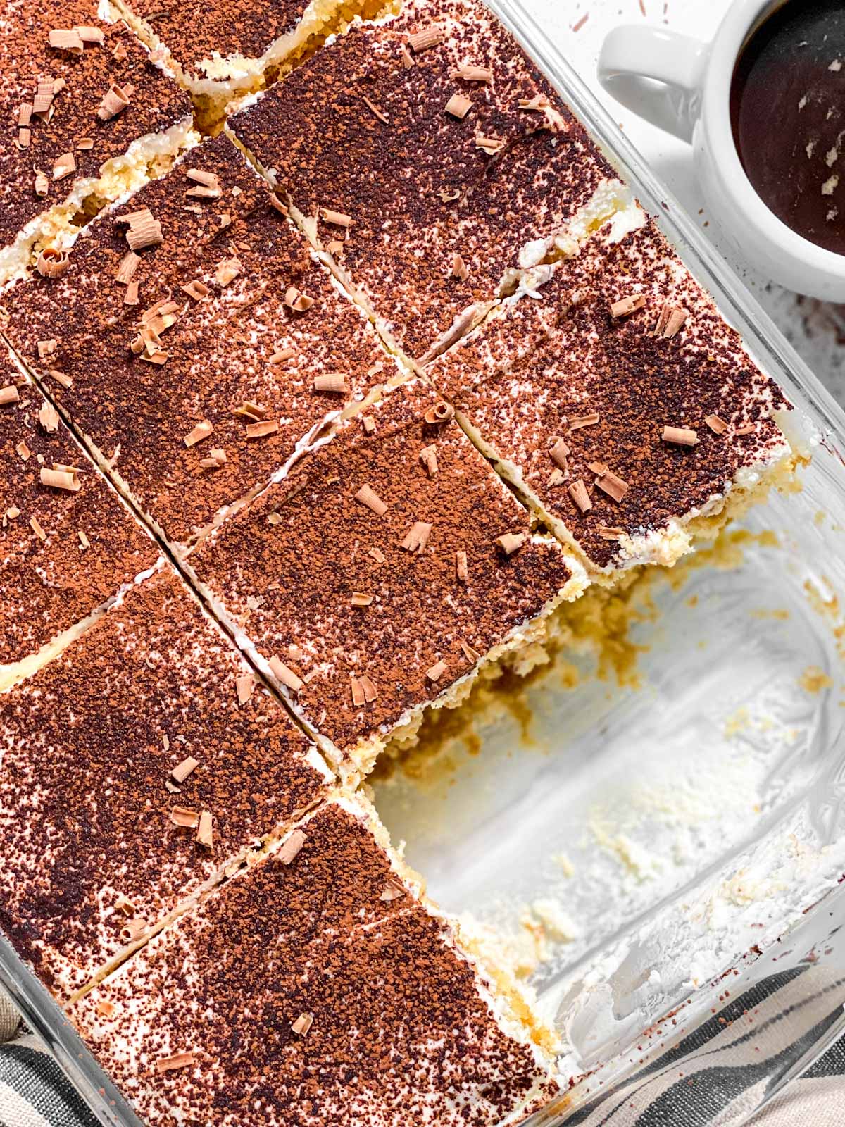 overhead view of sliced tiramisu in glass pan with two slices removed