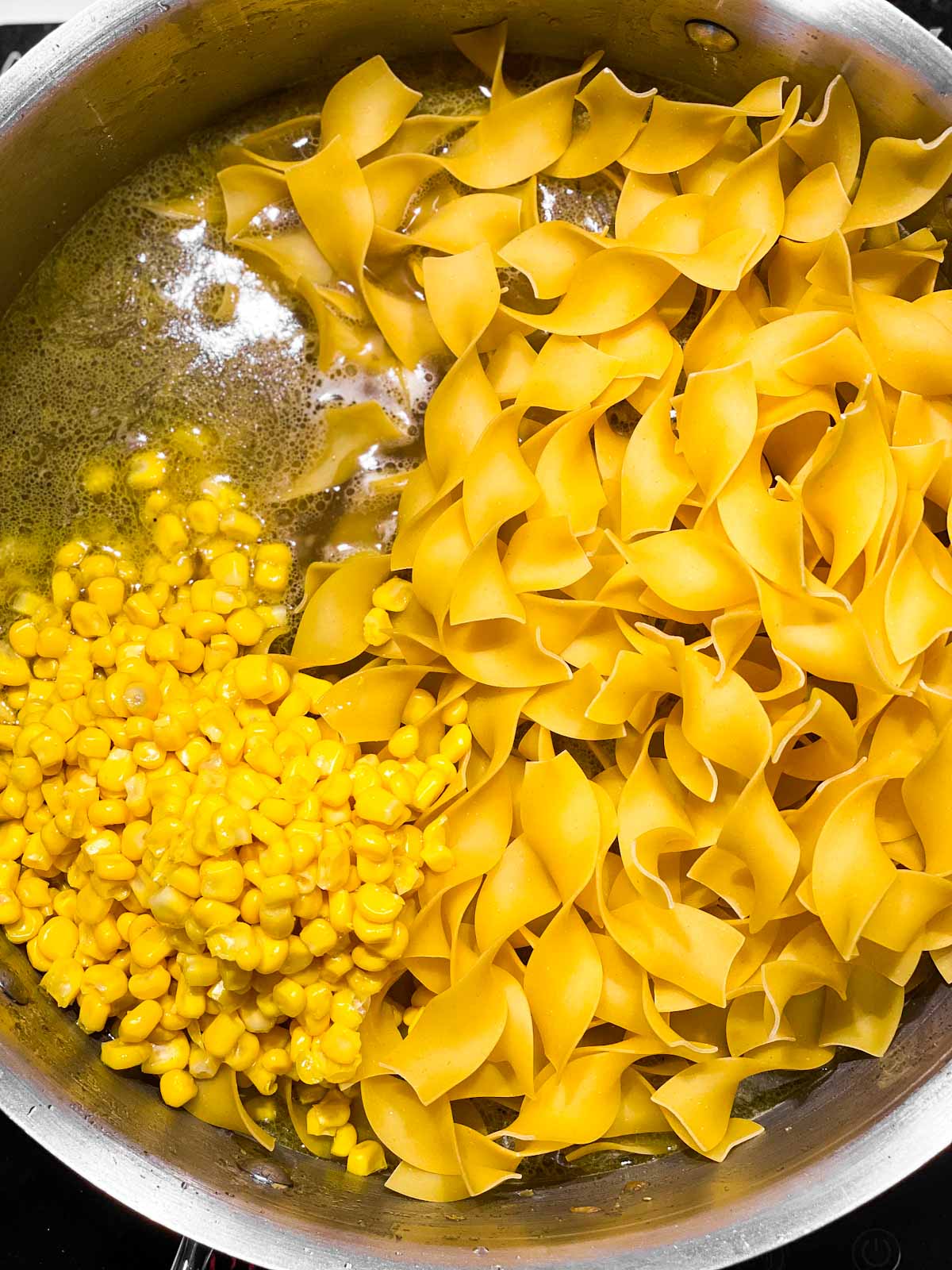 overhead view of pan with broth, uncooked noodles and corn