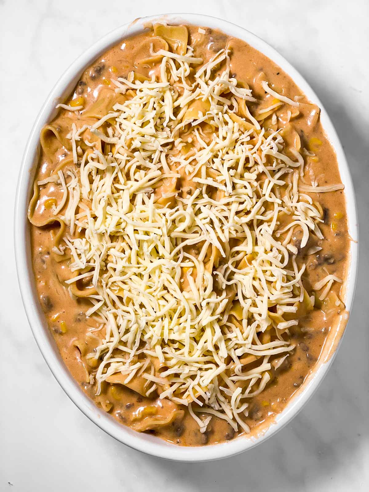 hamburger noodle mixture topped with shredded cheese in oval casserole dish