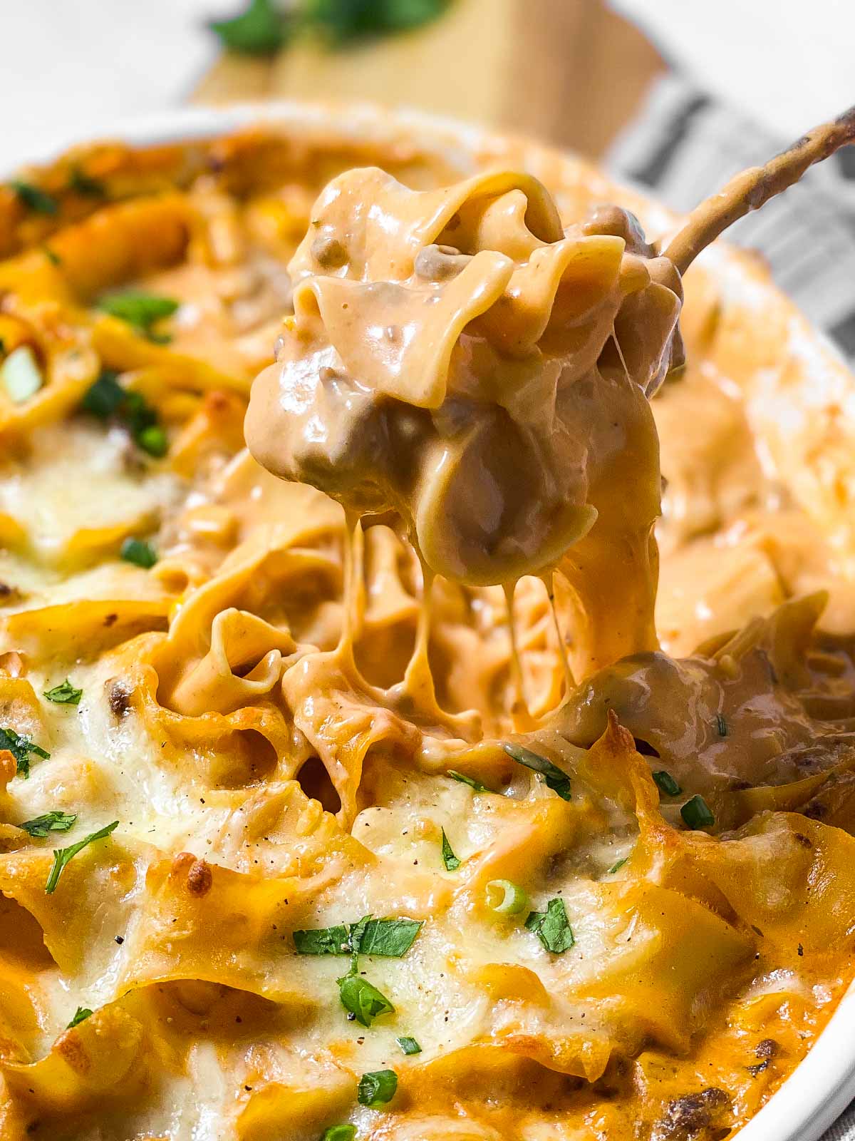 spoon scooping hamburger noodle casserole from white casserole dish