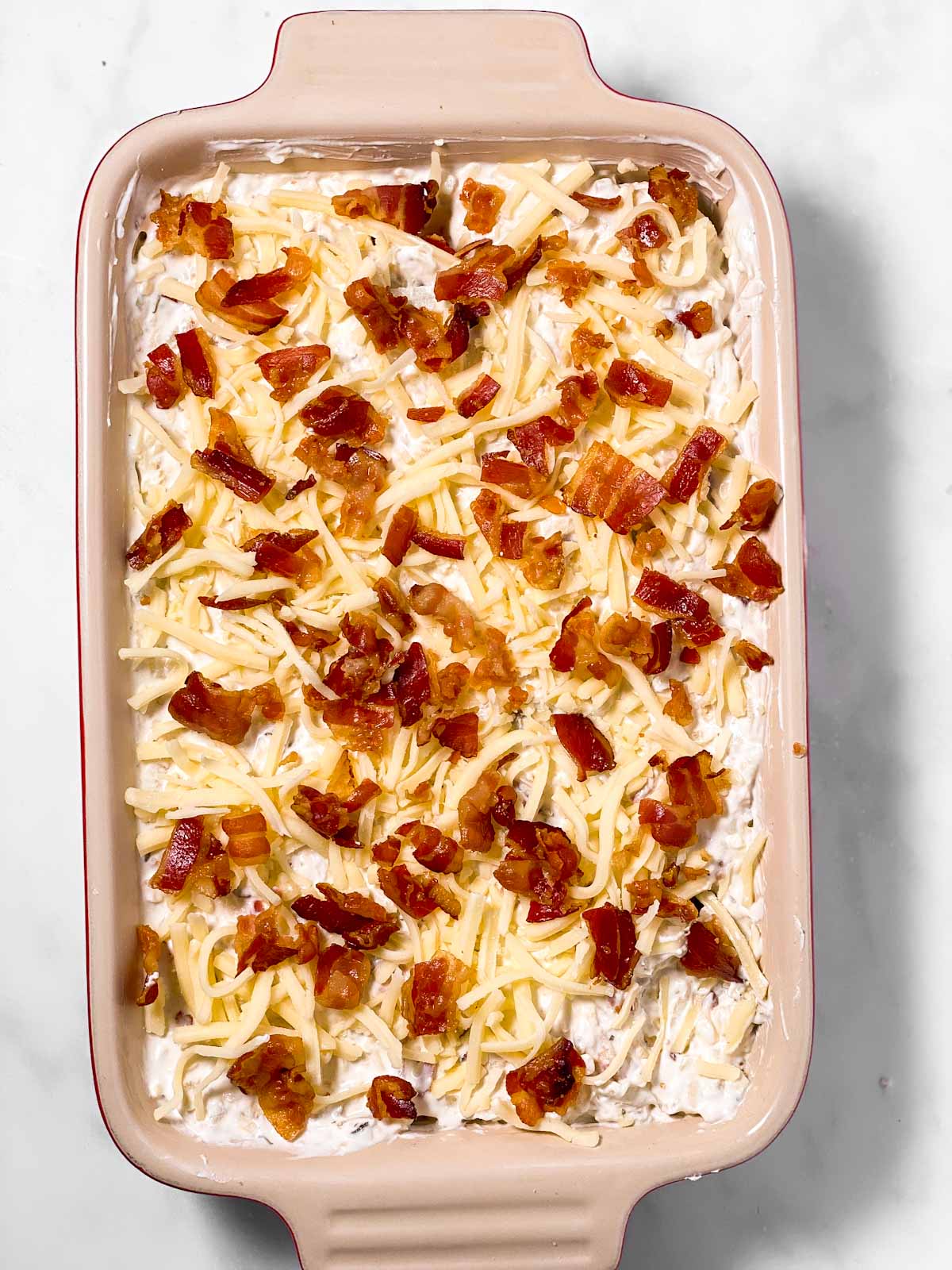 unbaked onion dip in rectangular casserole dish topped with bacon and cheese