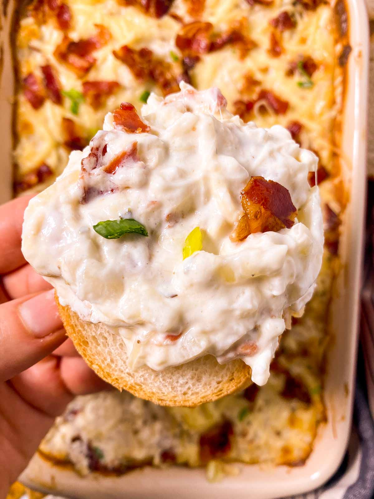 female hand holding bread slice with hot onion dip