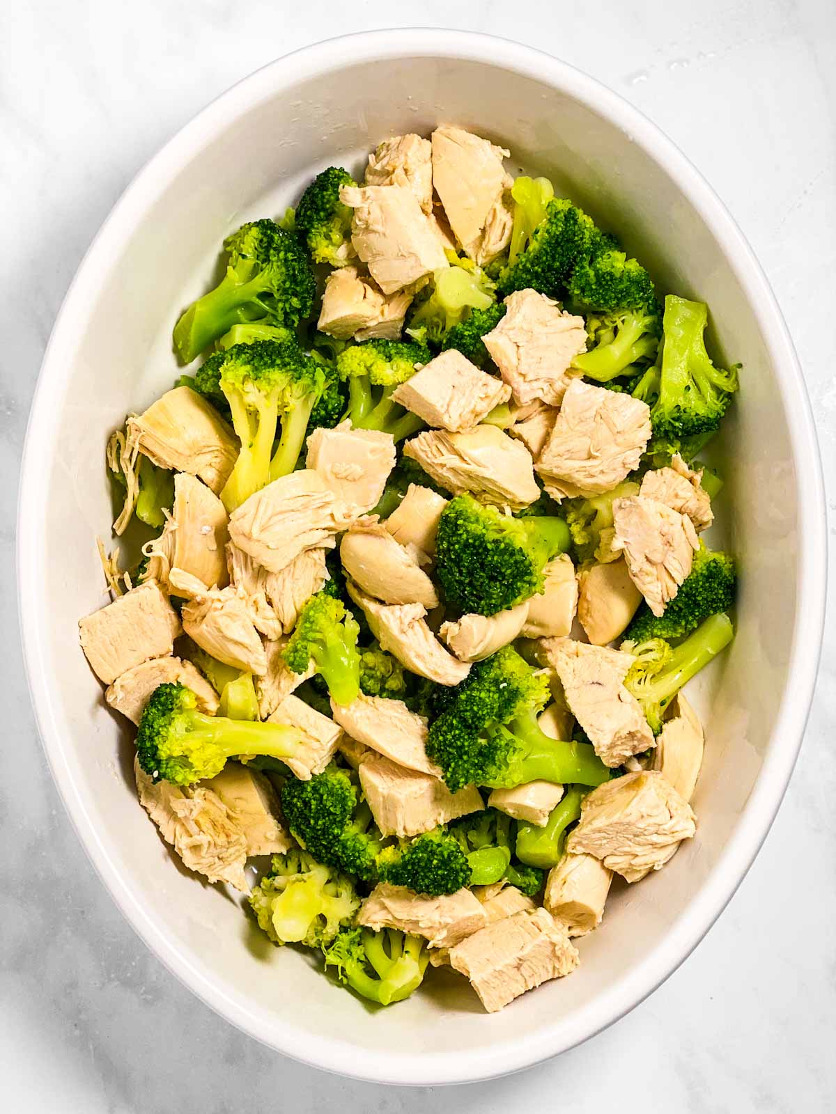cooked, diced chicken and broccoli in white oval casserole dish