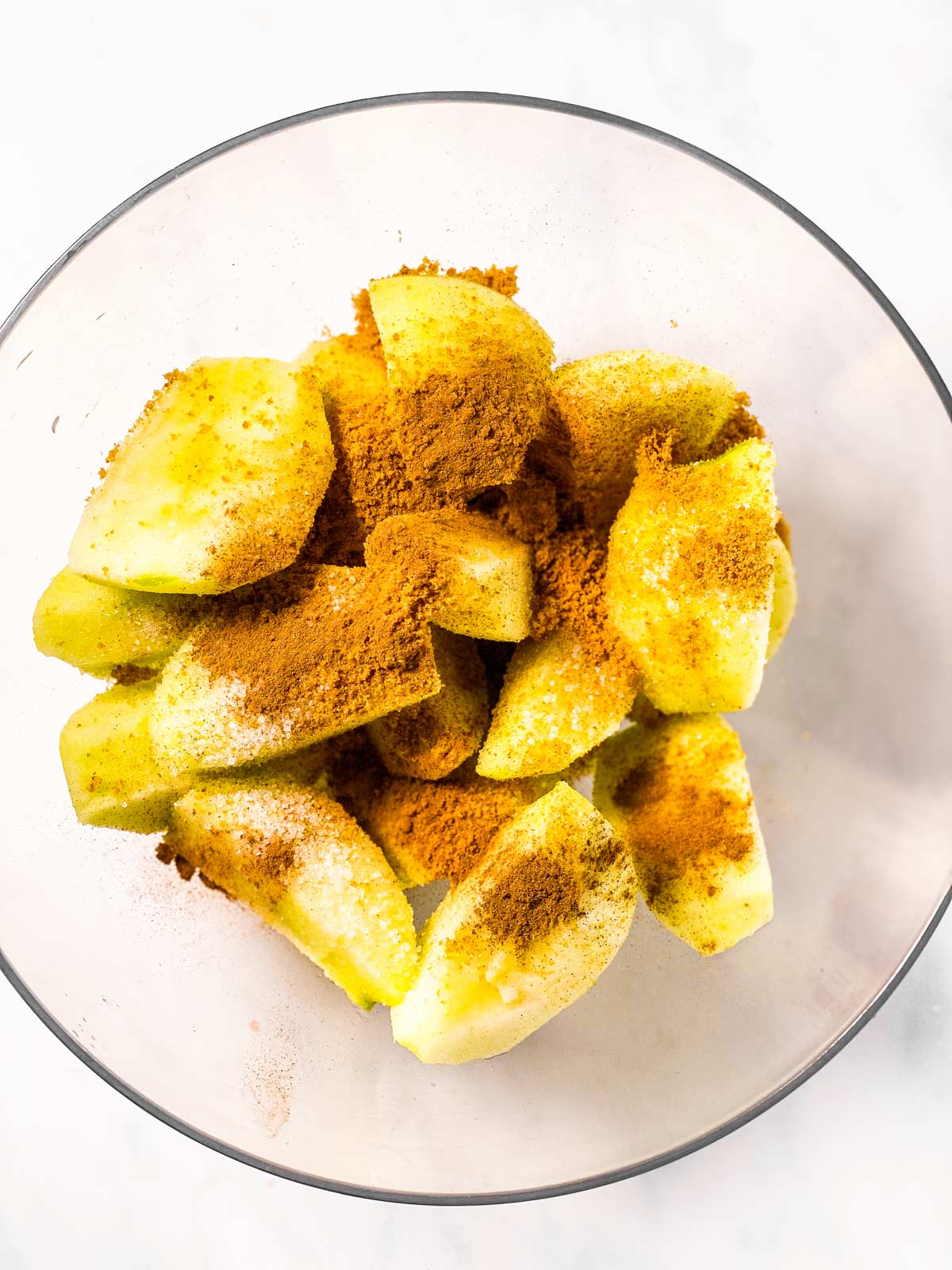 sliced apples in glass bowl with cinnamon and sugar