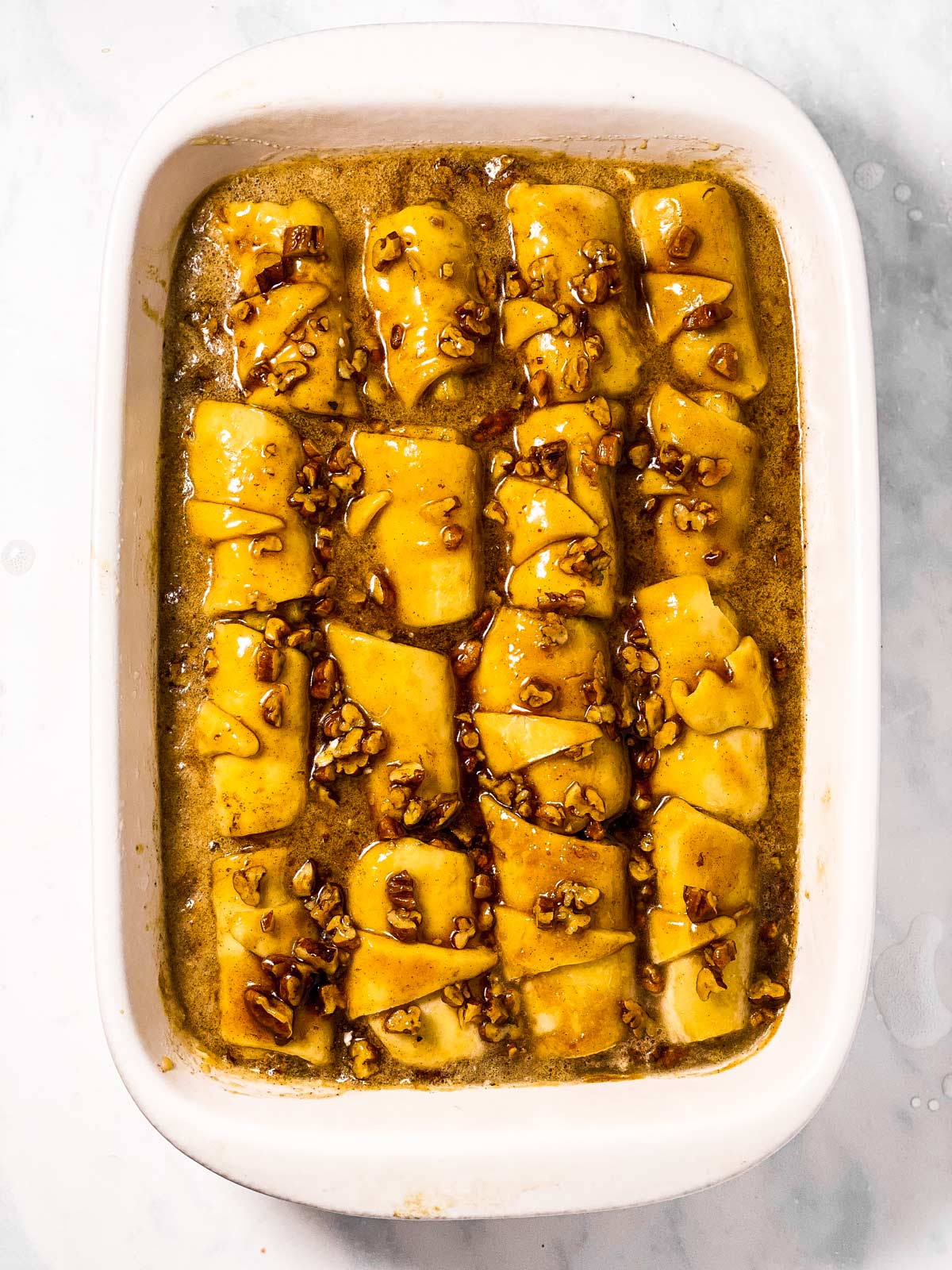 unbaked apple dumplings in pan surrounded by caramel sauce