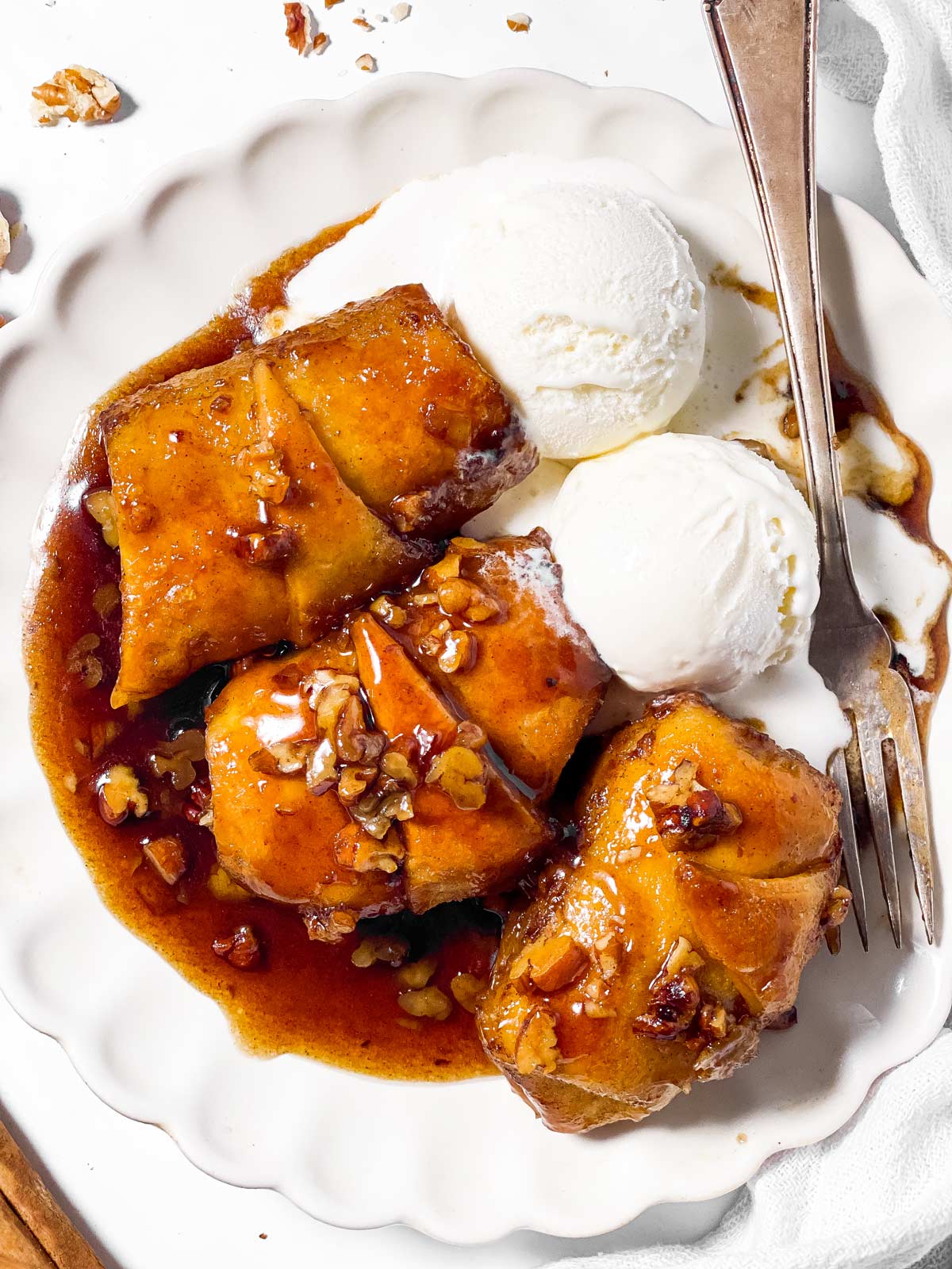 overhead view of three apple dumplings on white plate with two scoops of ice cream