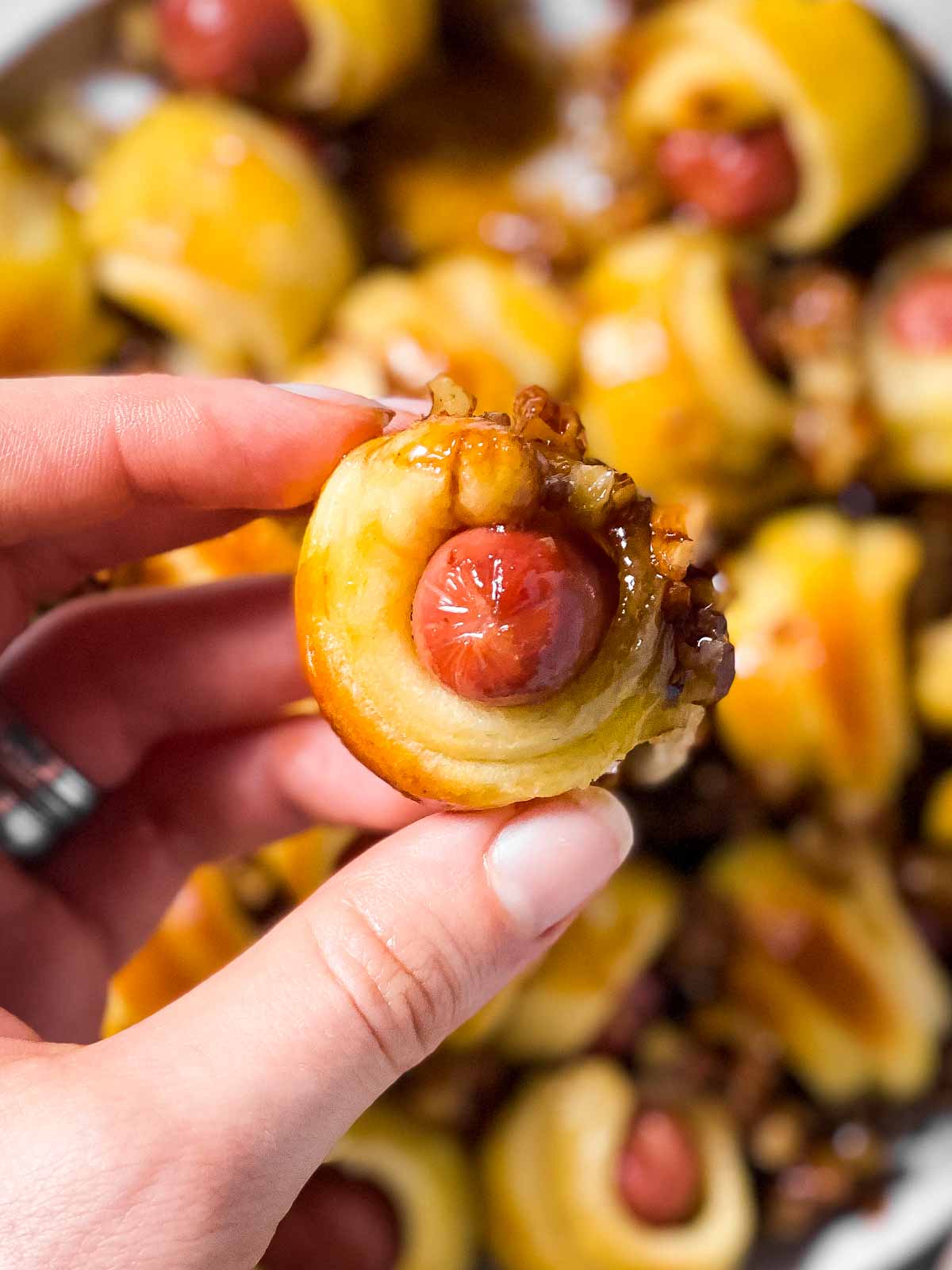 female hand holding a sticky pecan little smokie in crescent roll