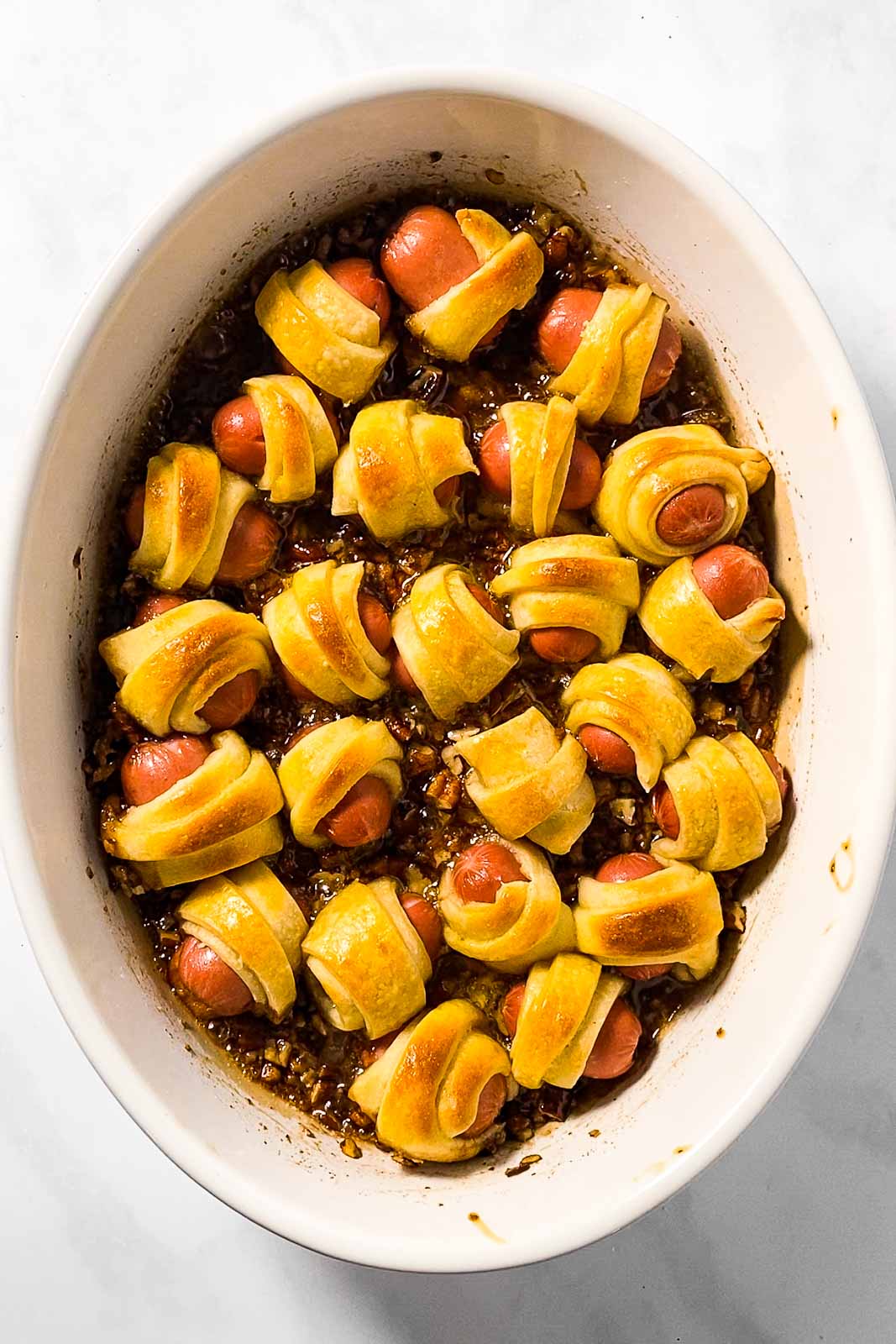 caramelized little smokies in crescent roll dough in white oval casserole dish