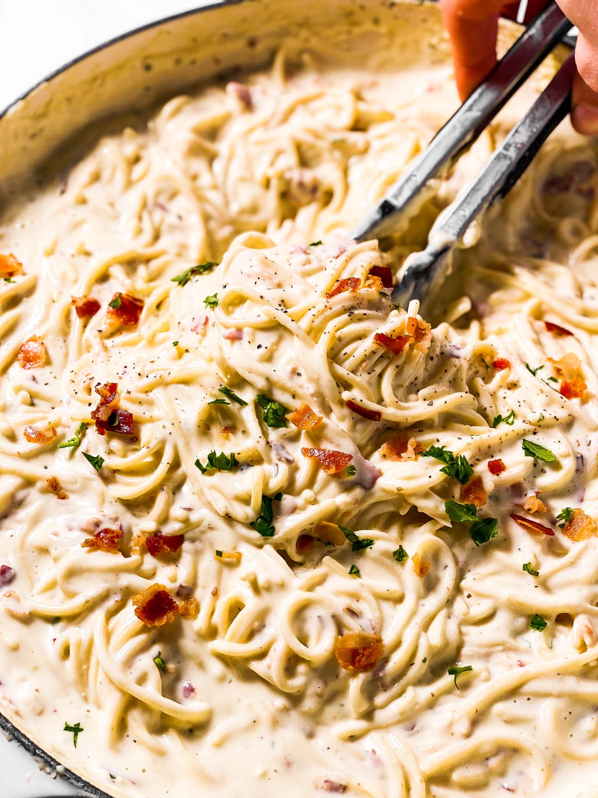 frontal close up view of kitchen tongs in pan of cream cheese pasta