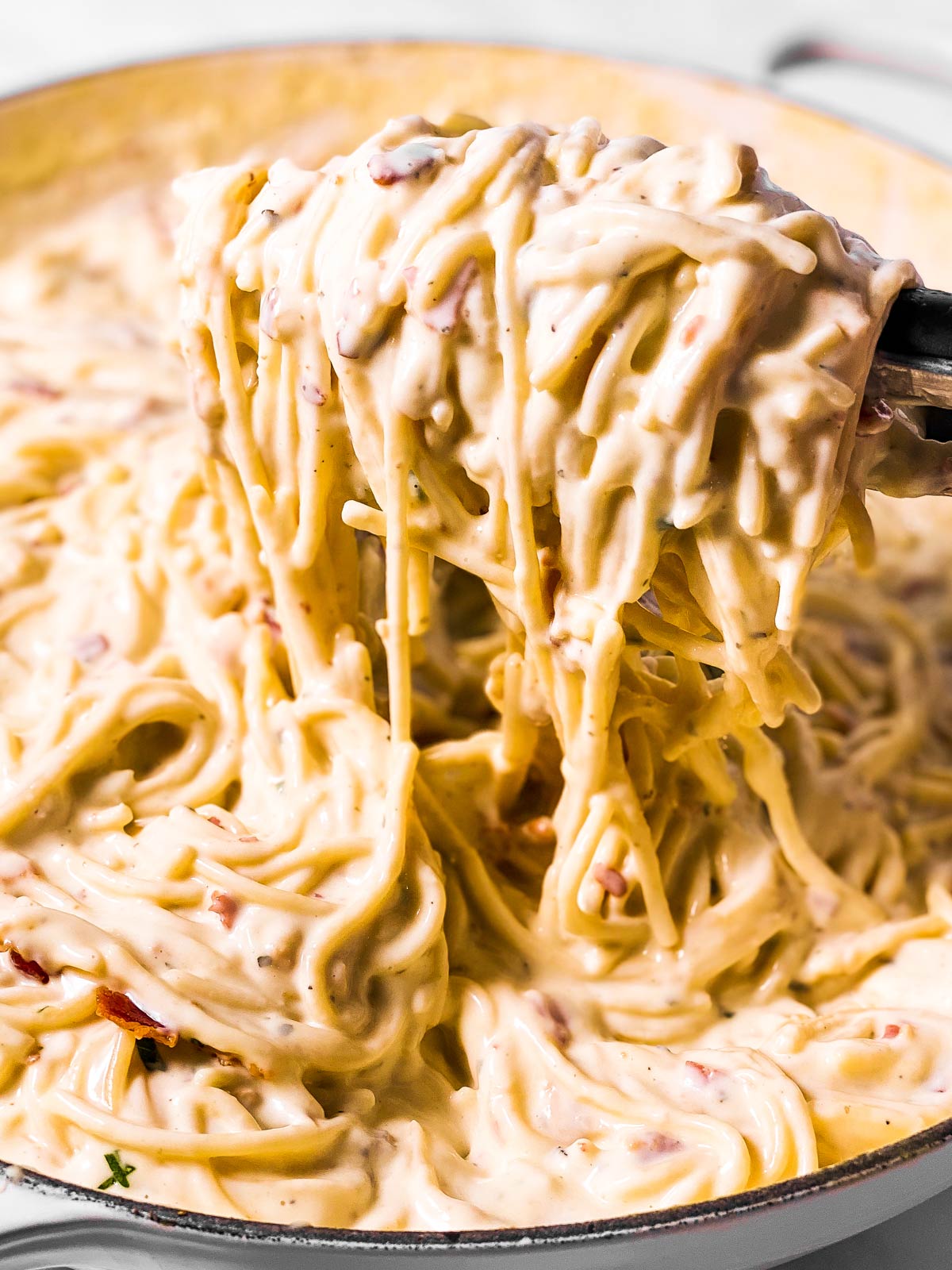 kitchen tongs scooping cream cheese pasta from skillet