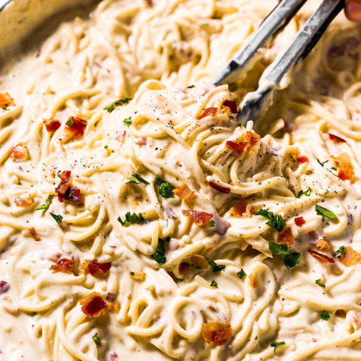 frontal close up view of kitchen tongs in pan of cream cheese pasta