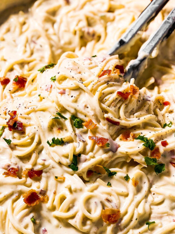 frontal close up view of kitchen tongs in pan of cream cheese pasta