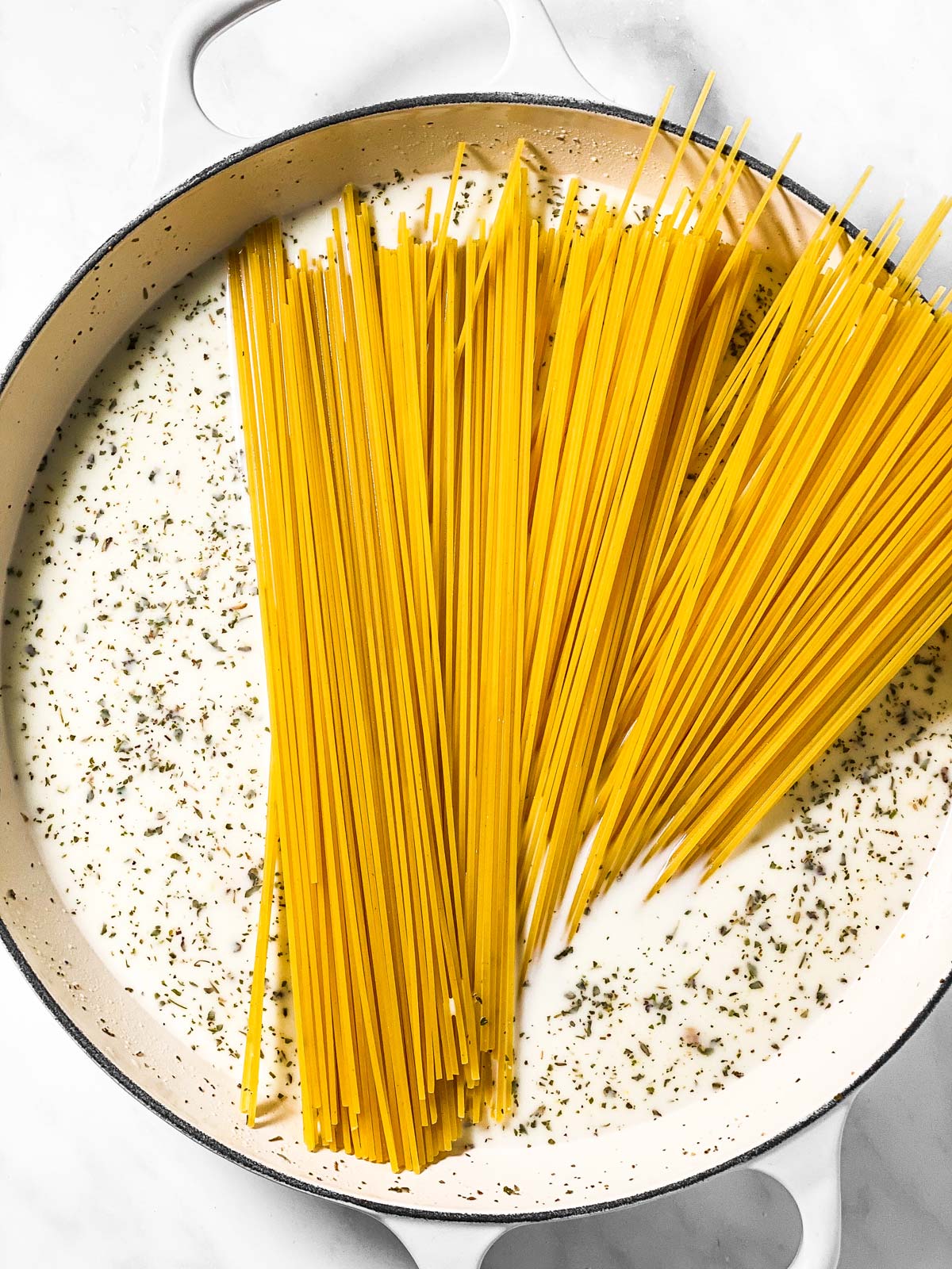 seasoned milk and uncooked spaghetti in large white cast iron skillet