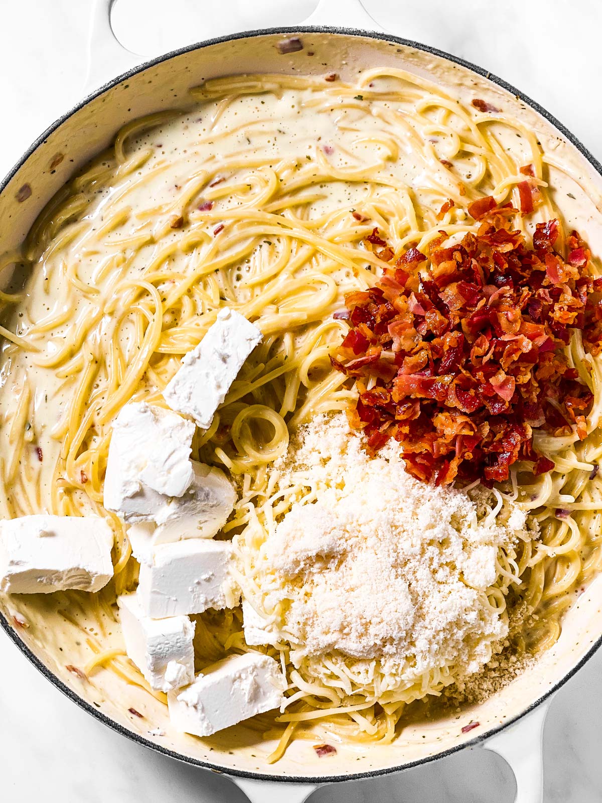 diced cream cheese, crumbled bacon and parmesan cheese on top of creamy spaghetti in sauté pan