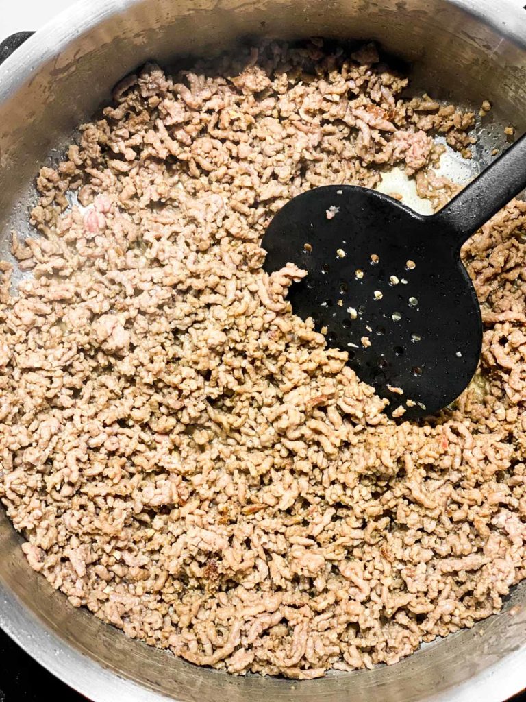 browned ground beef in skillet with black cooking spoon