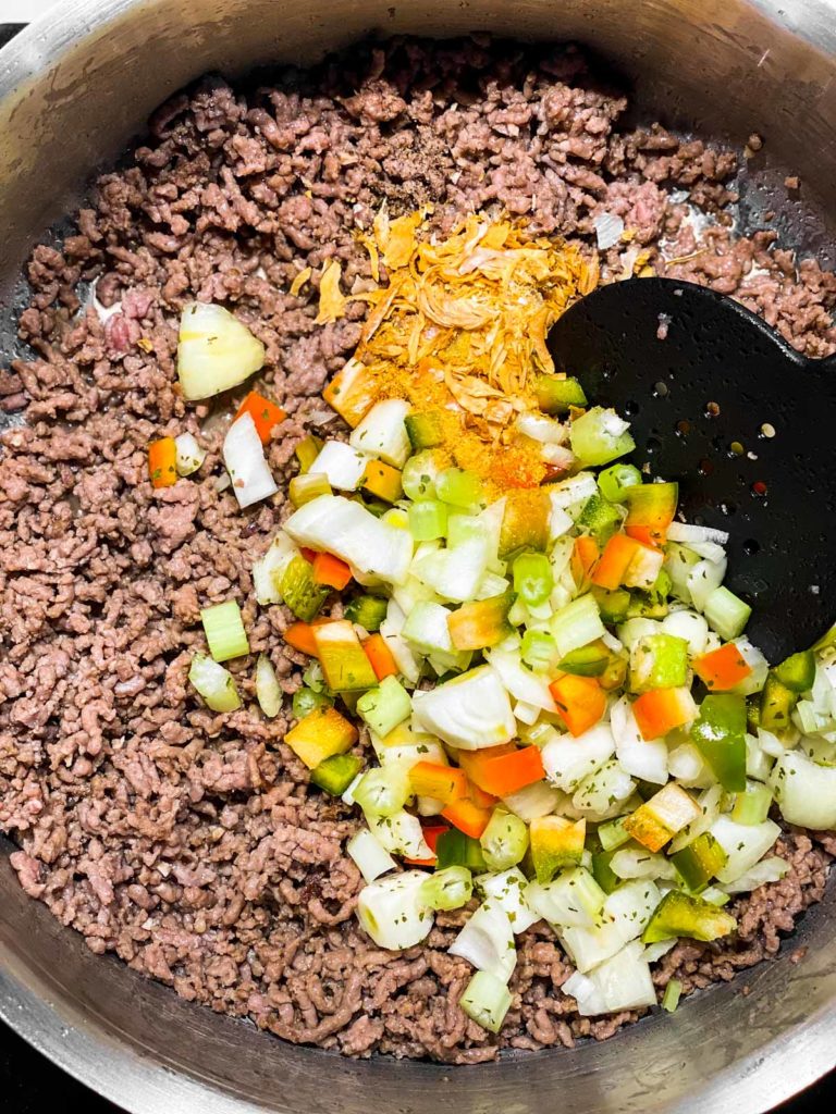 browned ground beef in skillet with seasoning blend, seasoning and black cooking spoon