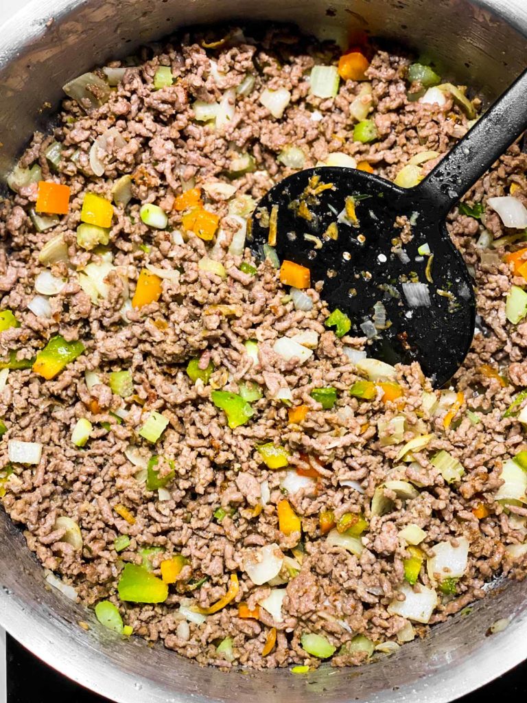 browned ground beef in skillet with cooked seasoning blend and black cooking spoon