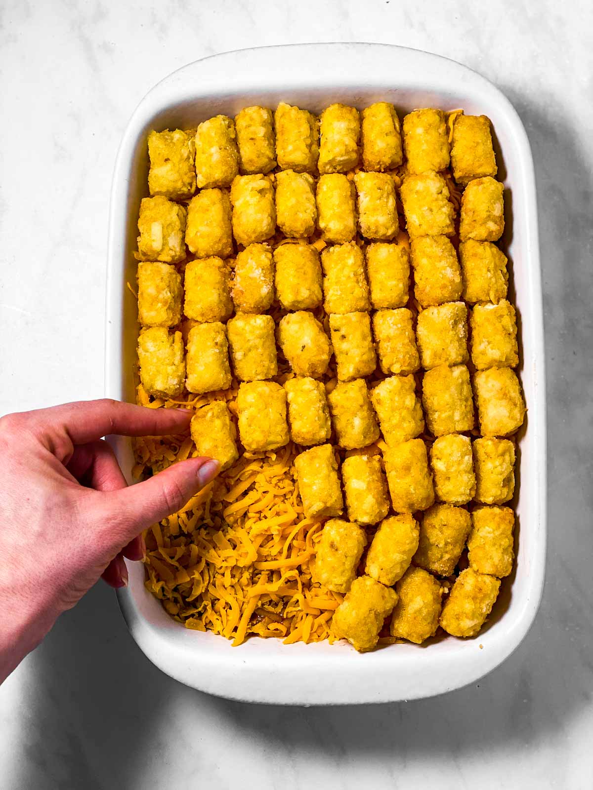 female hand placing tater tot on top of casserole