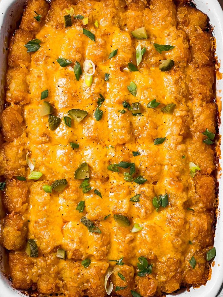 overhead closeup of sloppy joe tater tot casserole garnished with green onion, pickles and parsley